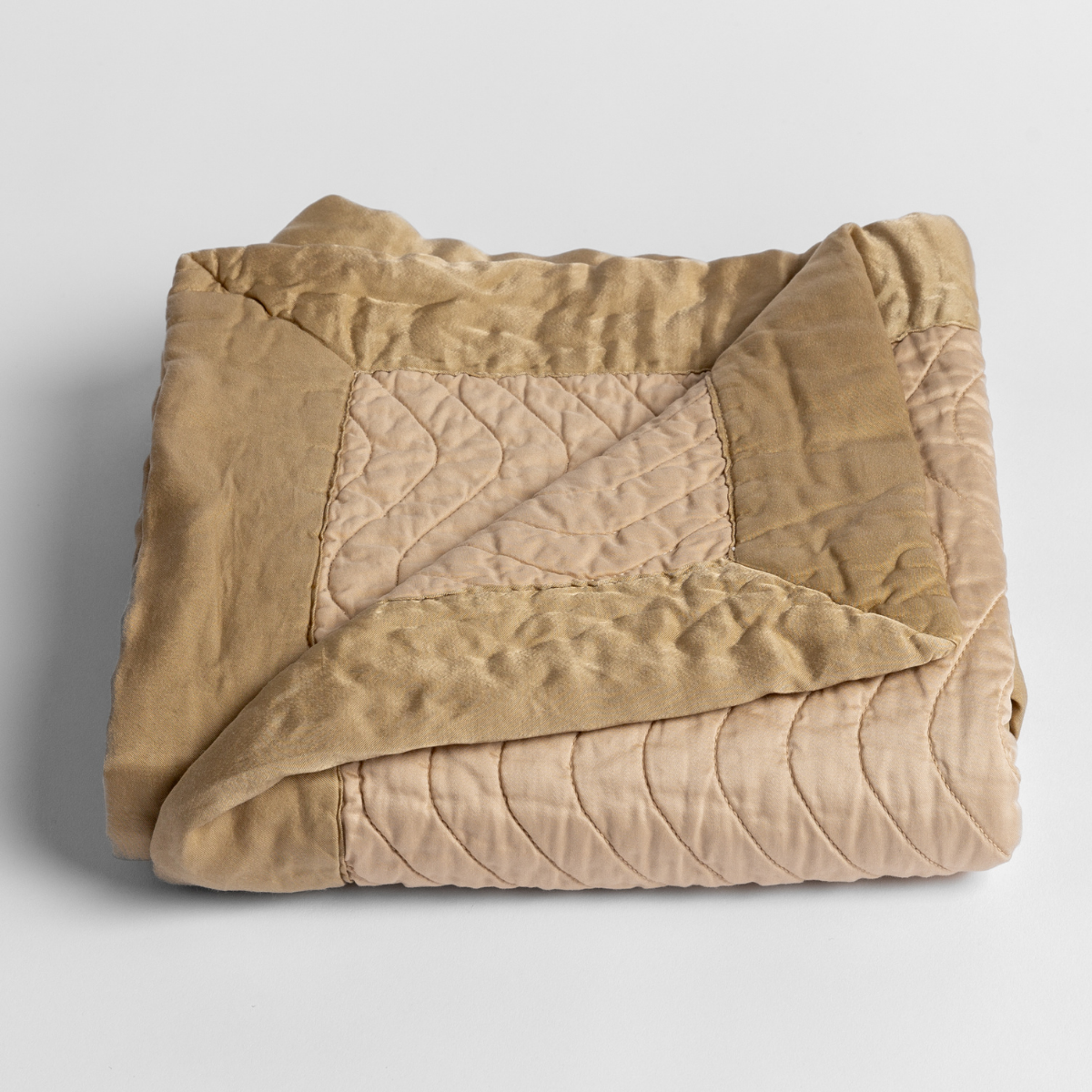Honeycomb: a folded quilted cotton sateen baby blanket with its corner folded down to show the trim contrast - shot against a white background. 