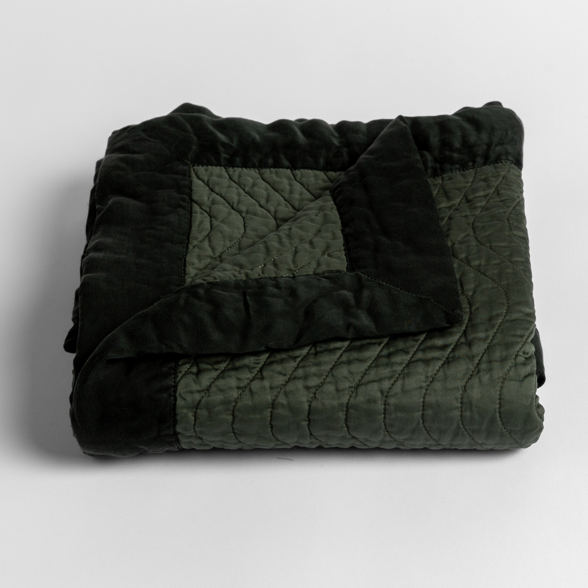 Juniper: a folded quilted cotton sateen baby blanket with its corner folded down to show the trim contrast - shot against a white background. 