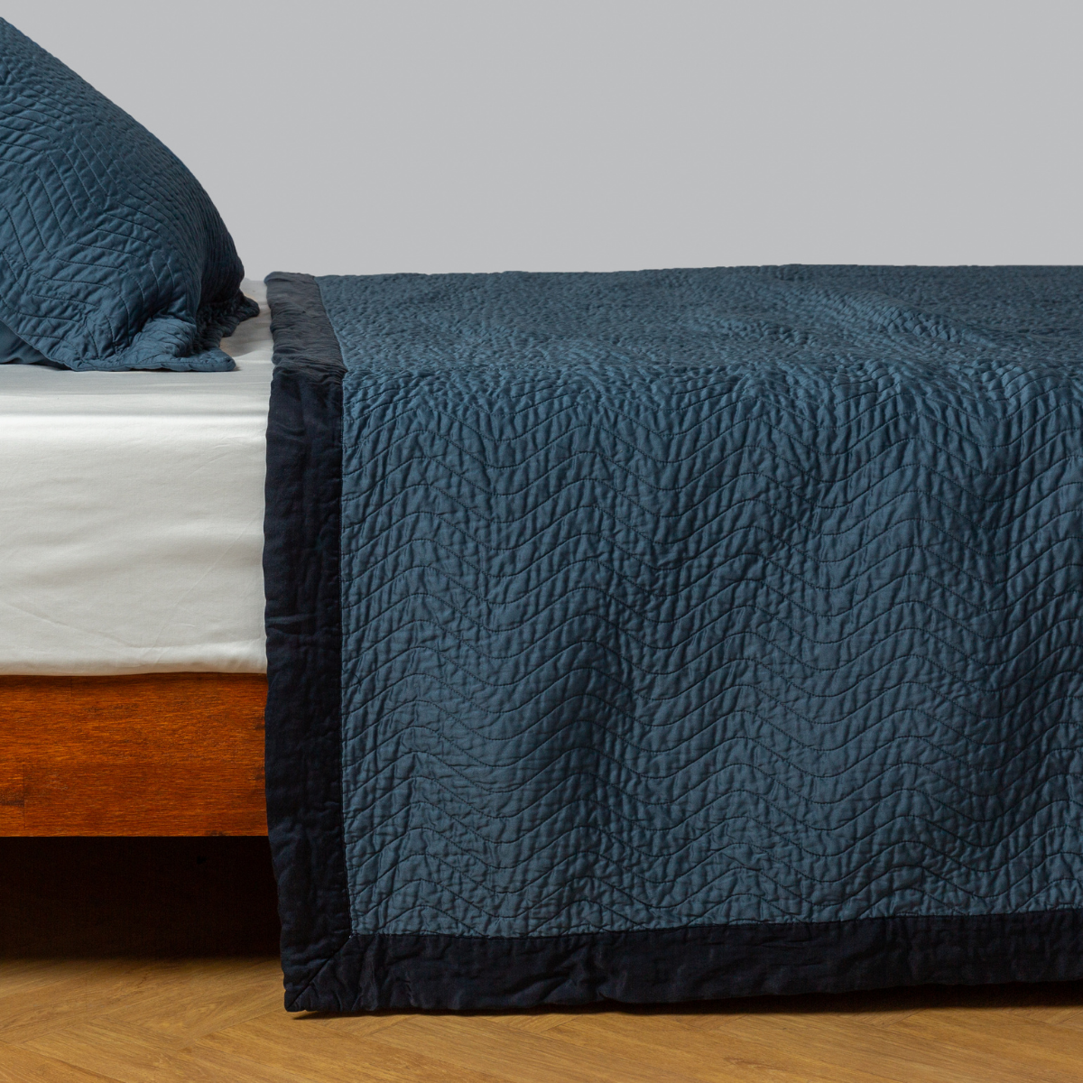 Midnight: quilted cotton sateen coverlet with matching sham on a winter white fitted sheet - side view. 