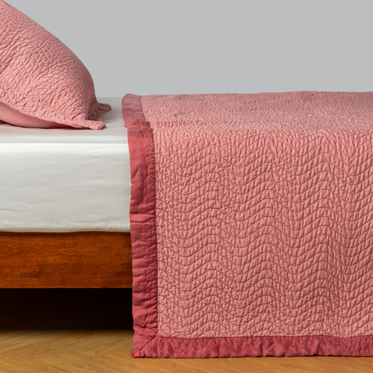 Poppy: quilted cotton sateen coverlet with matching sham on a winter white fitted sheet - side view. 
