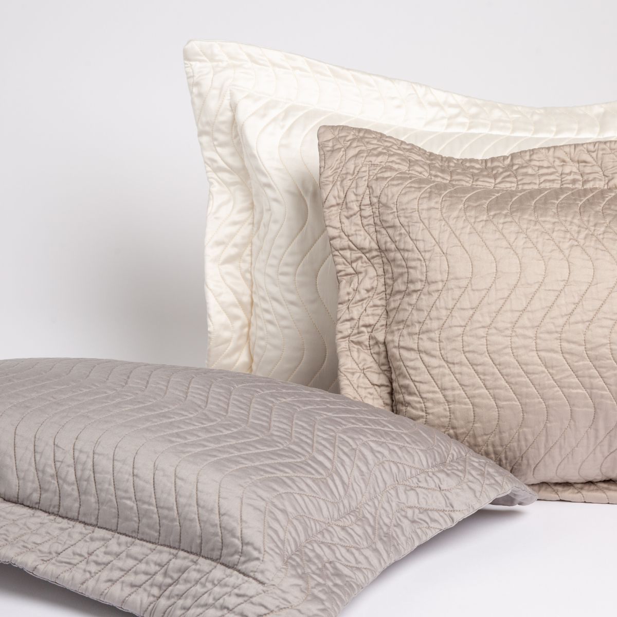 [allvariants]: a cluster of quilted cotton sateen throw pillows in neutral tones against a white background. 