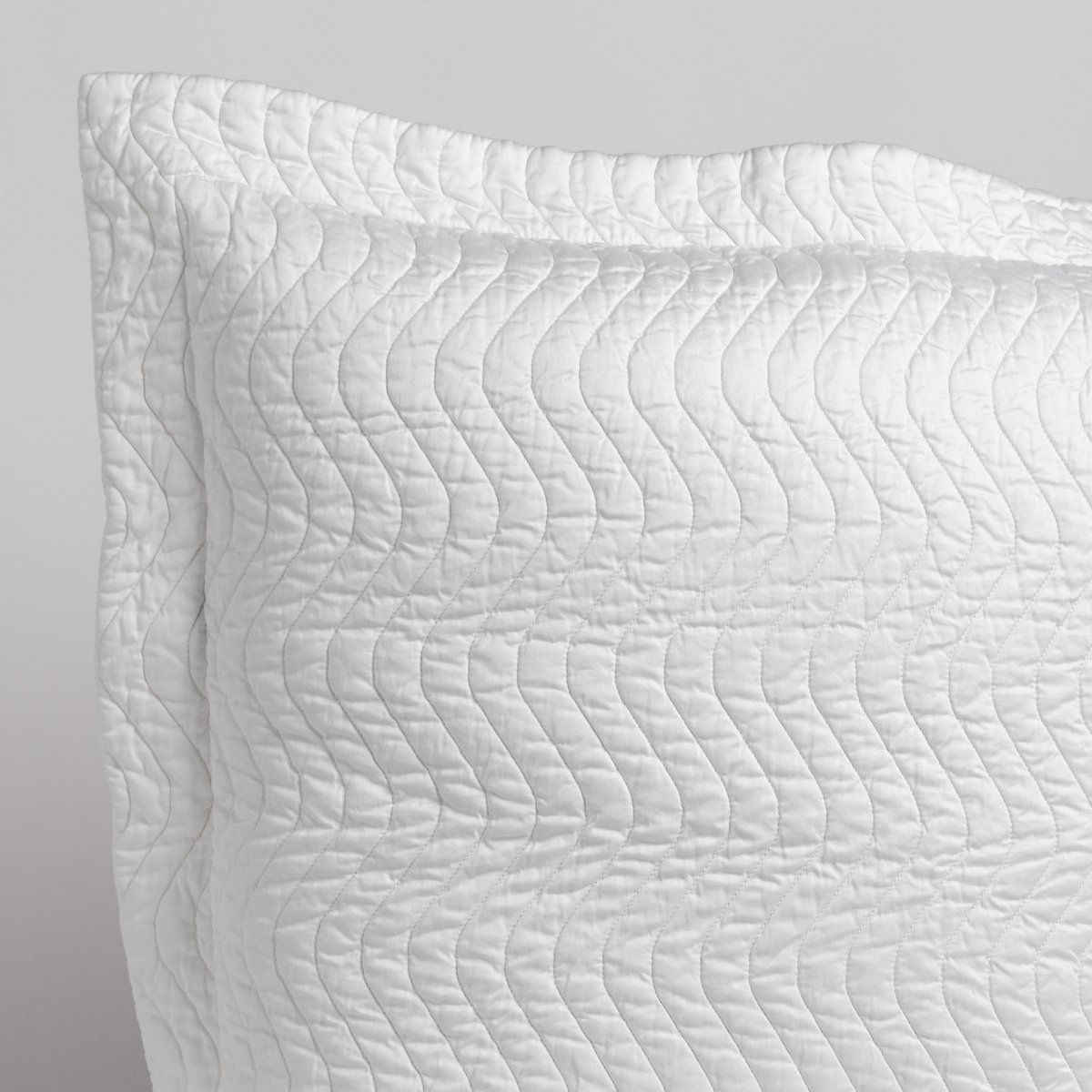 White: a close up of a pillow corner showing the flange framing quilted cotton sateen shot against a white background. 
