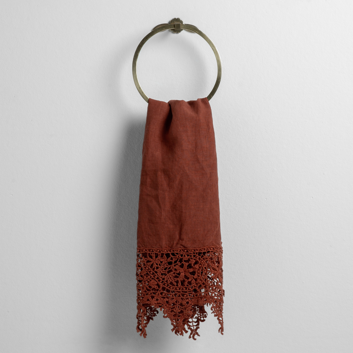 Autumn: A close-up of a Frida Guest Towel in Autumn, a rich terracotta tone, hanging from a round towel ring shown against a white background. 