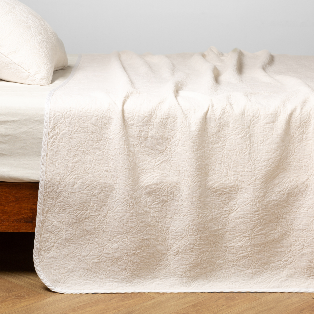 Winter White: side view of the chenille jacquard side of a bedspread with the cotton jacquard side showing on the matching sham — shown with a winter white fitted sheet. 