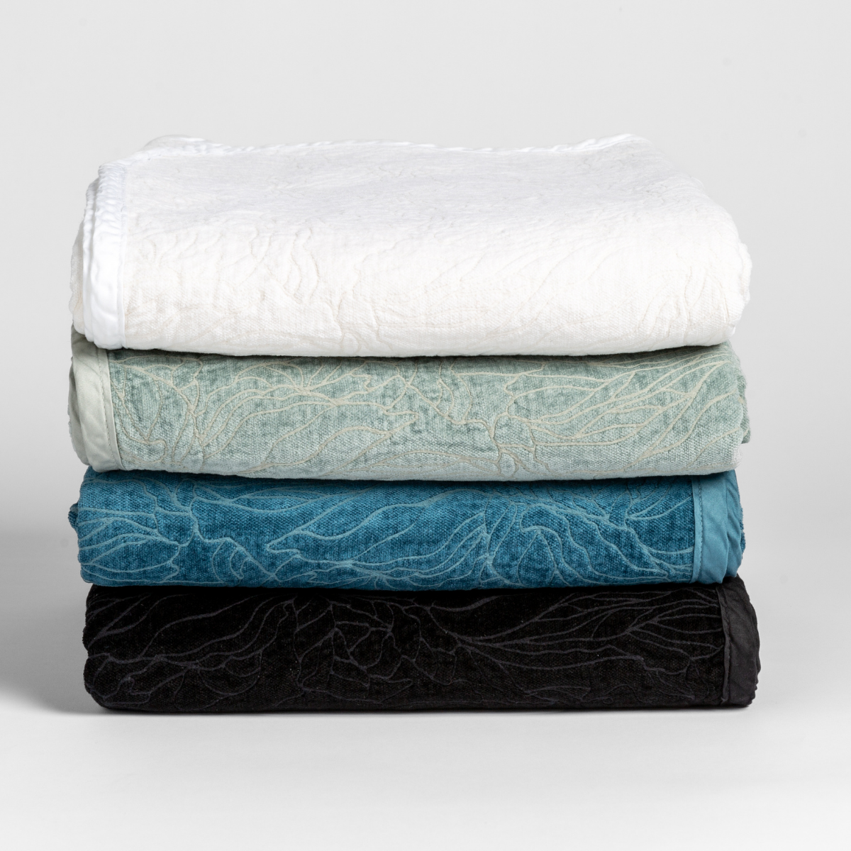 [allvariants]: a stack of four blankets folded with their chenille jacquard sides facing outward and the cotton sateen trim subtle and tonal. 