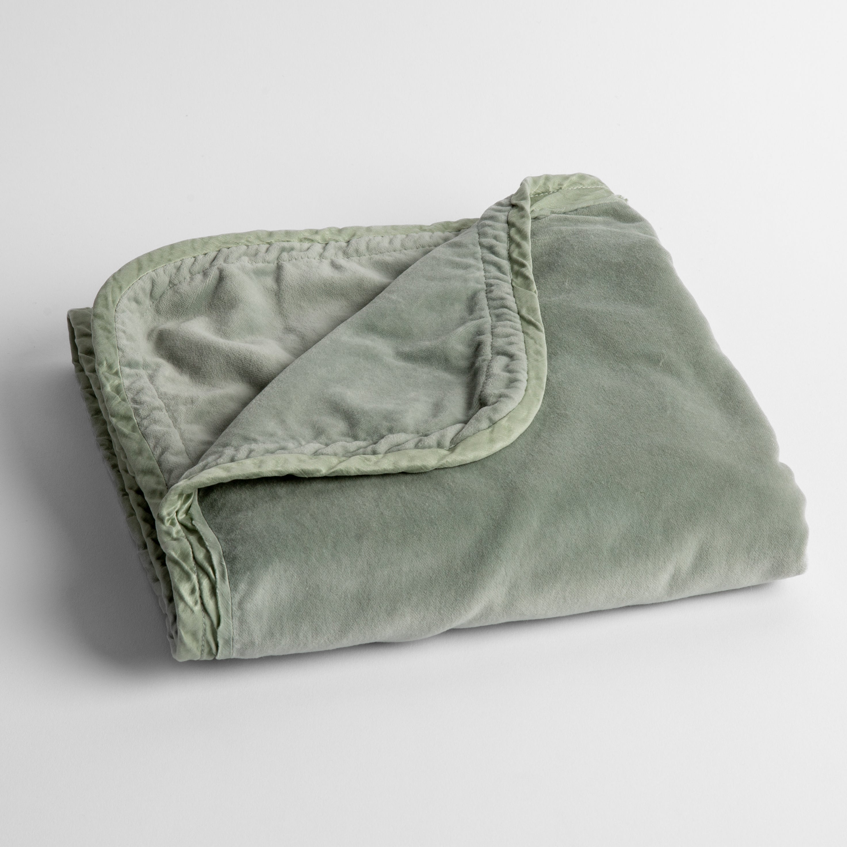 Eucalyptus:  cotton velvet baby blanket trimmed with charmeuse, folded with a covern folded back to show trim contrast; shot overhead and at a slight angle against a white background. 