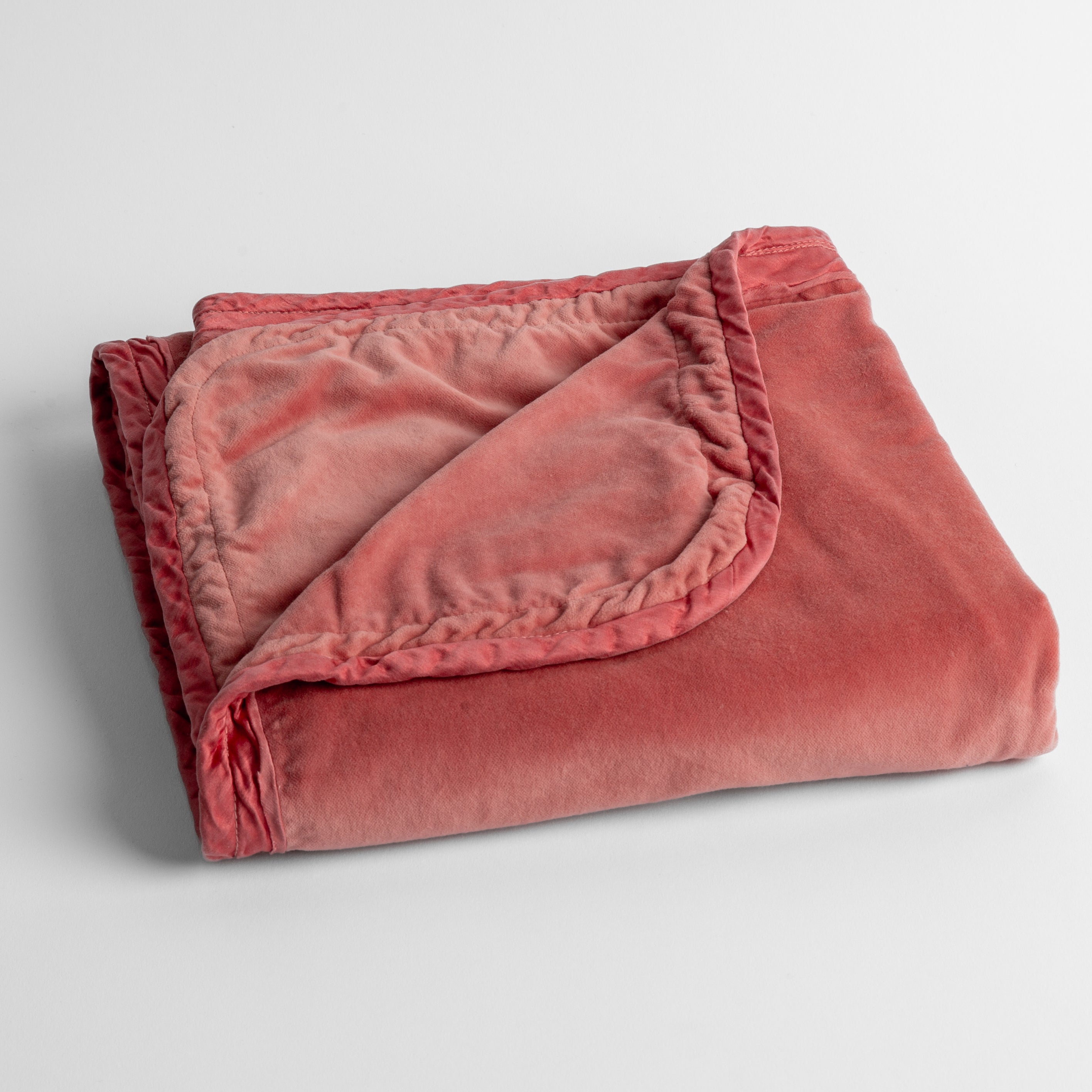 Poppy: cotton velvet baby blanket trimmed with charmeuse, folded with a covern folded back to show trim contrast; shot overhead and at a slight angle against a white background. 