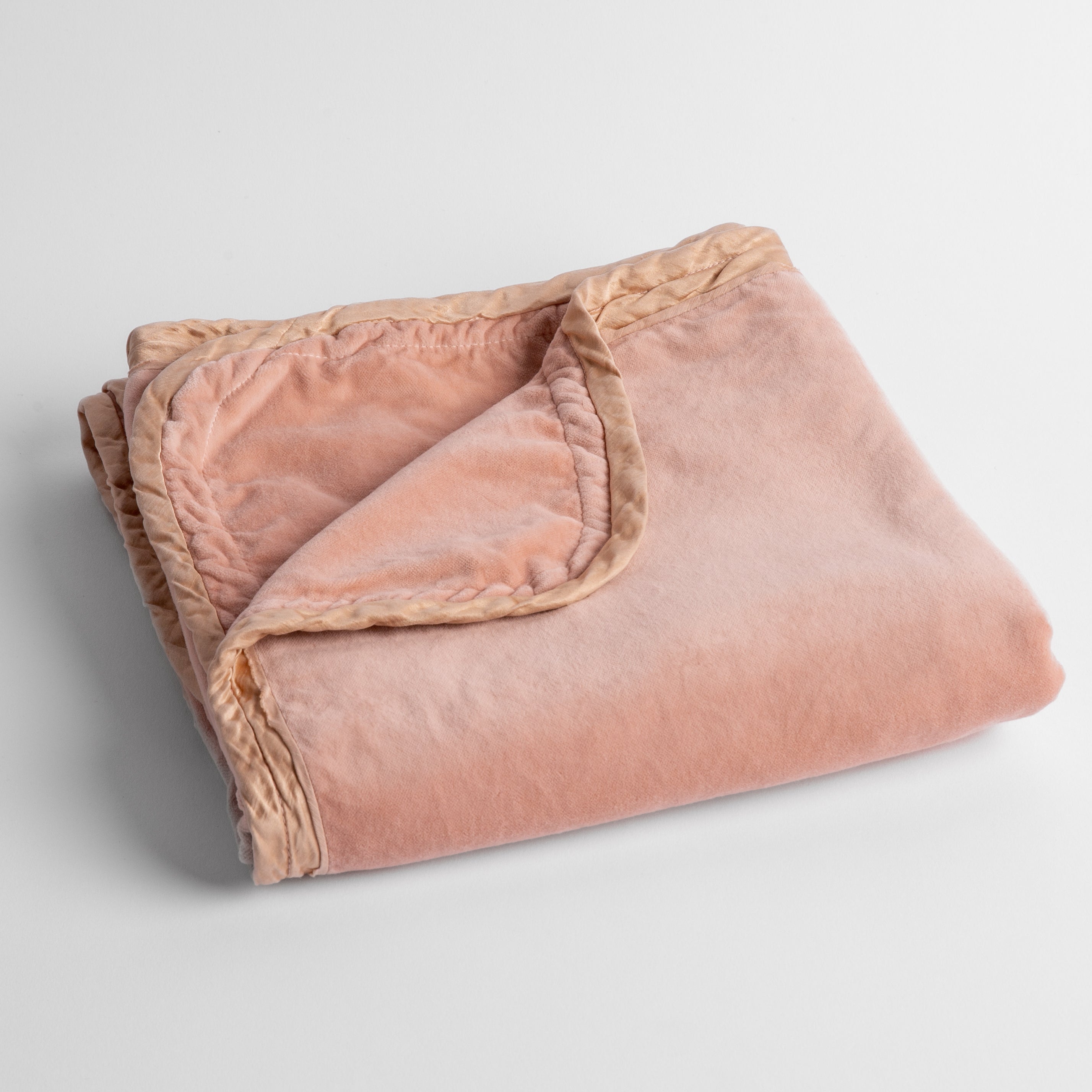 Rouge: cotton velvet baby blanket trimmed with charmeuse, folded with a covern folded back to show trim contrast; shot overhead and at a slight angle against a white background. 