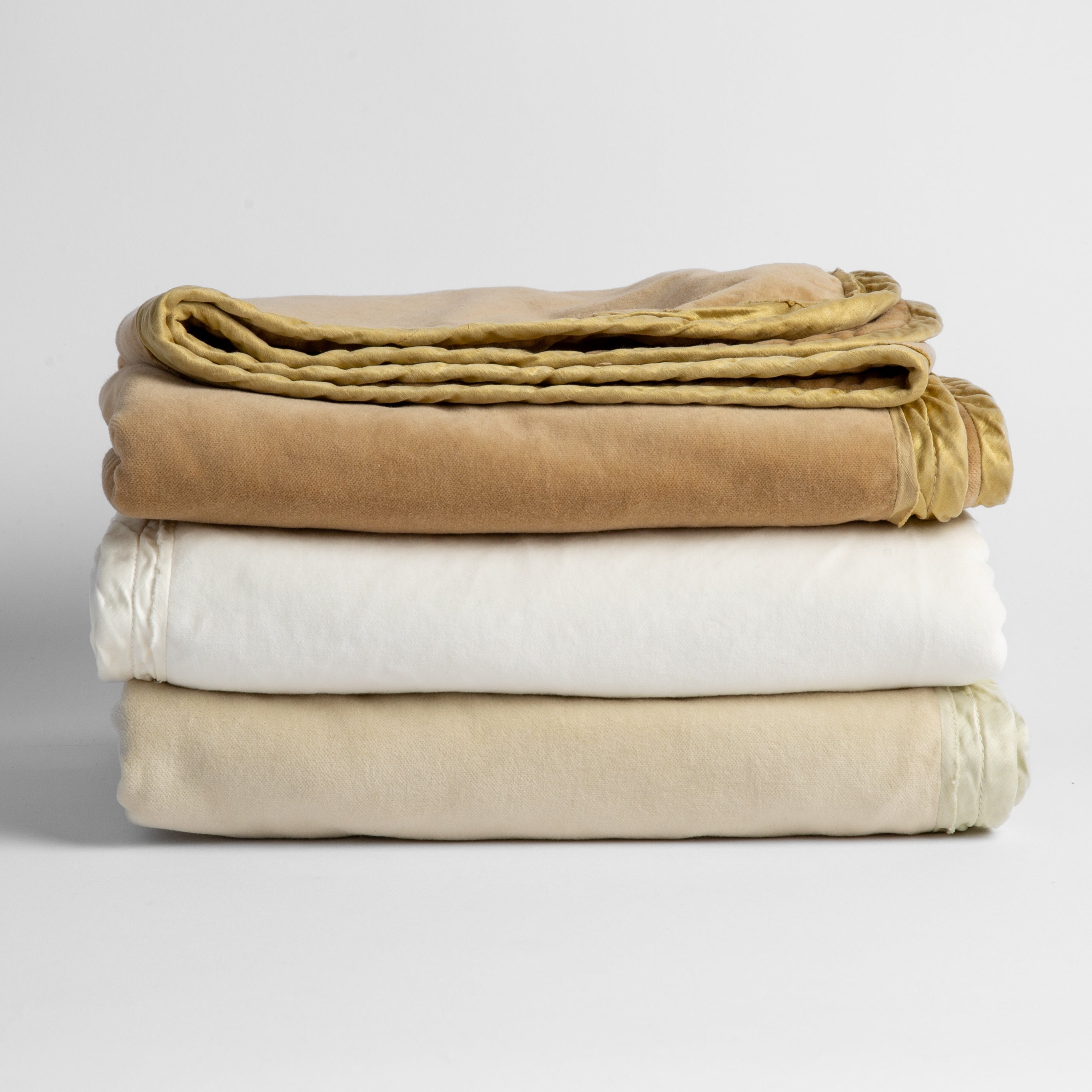 : stack of three cotton velvet baby blankets in neutral tones against a white background. 