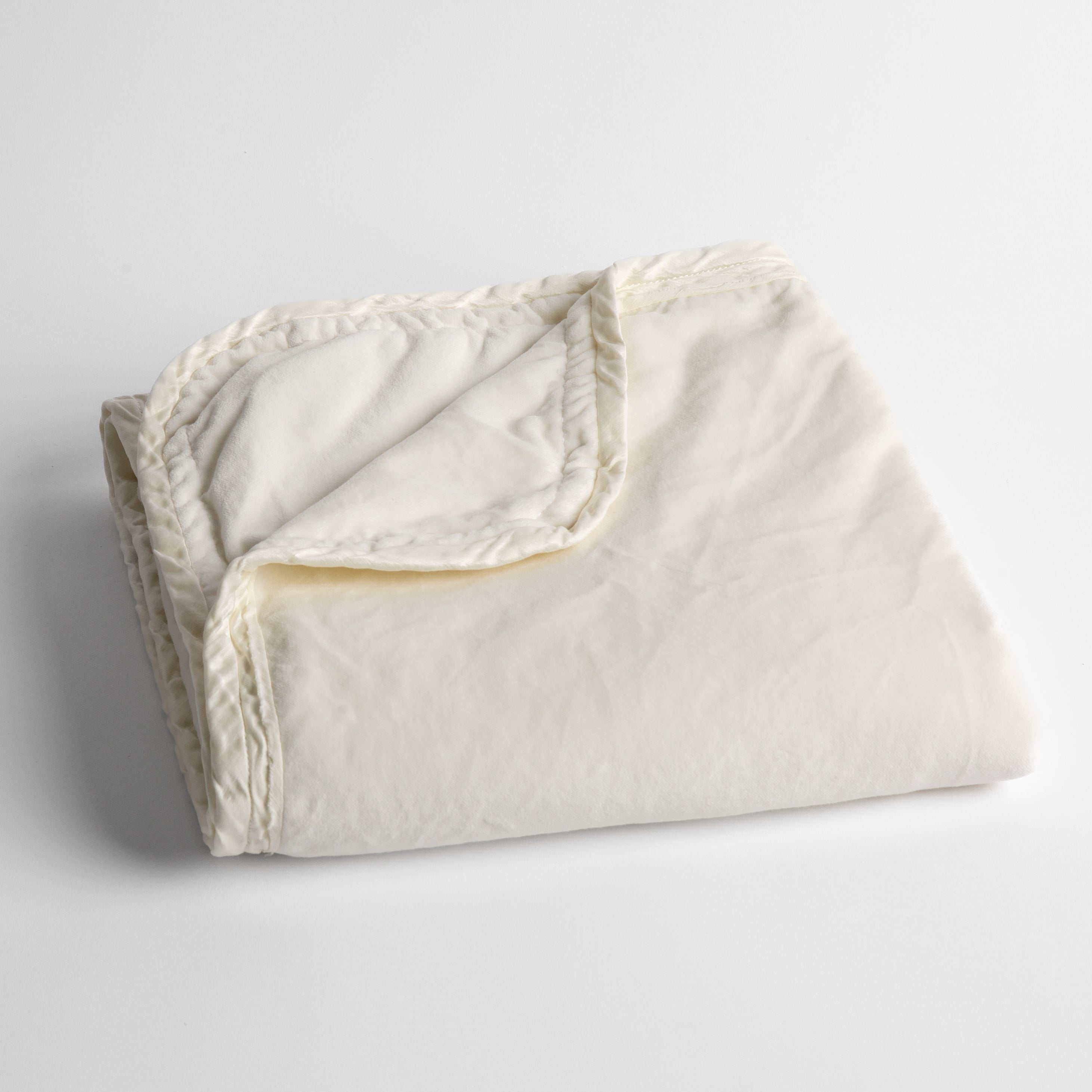 Winter White: cotton velvet baby blanket trimmed with charmeuse, folded with a covern folded back to show trim contrast; shot overhead and at a slight angle against a white background. 