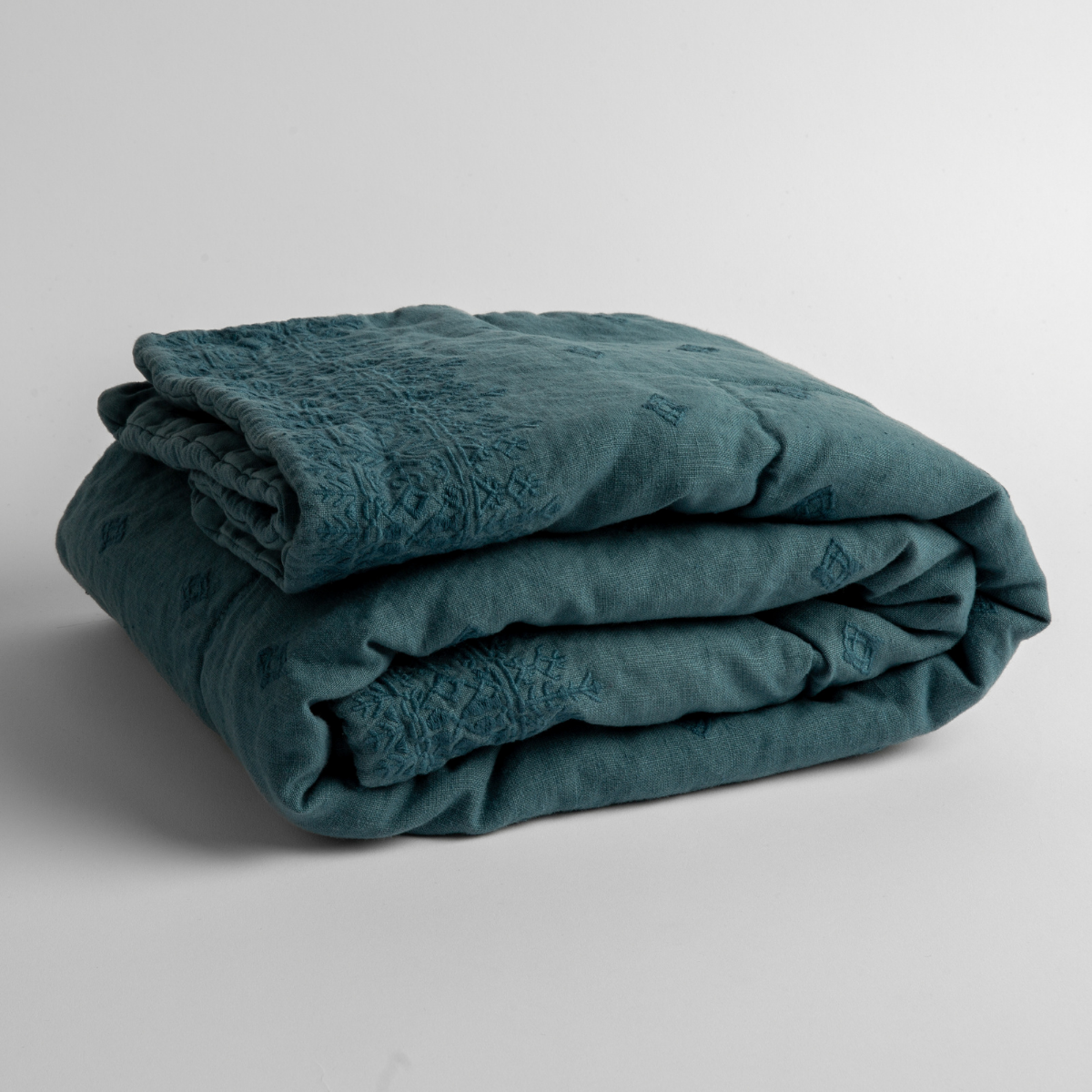 Cenote:  embroidered linen baby blanket folded and shown  overhead from a slight angle against a white background. 