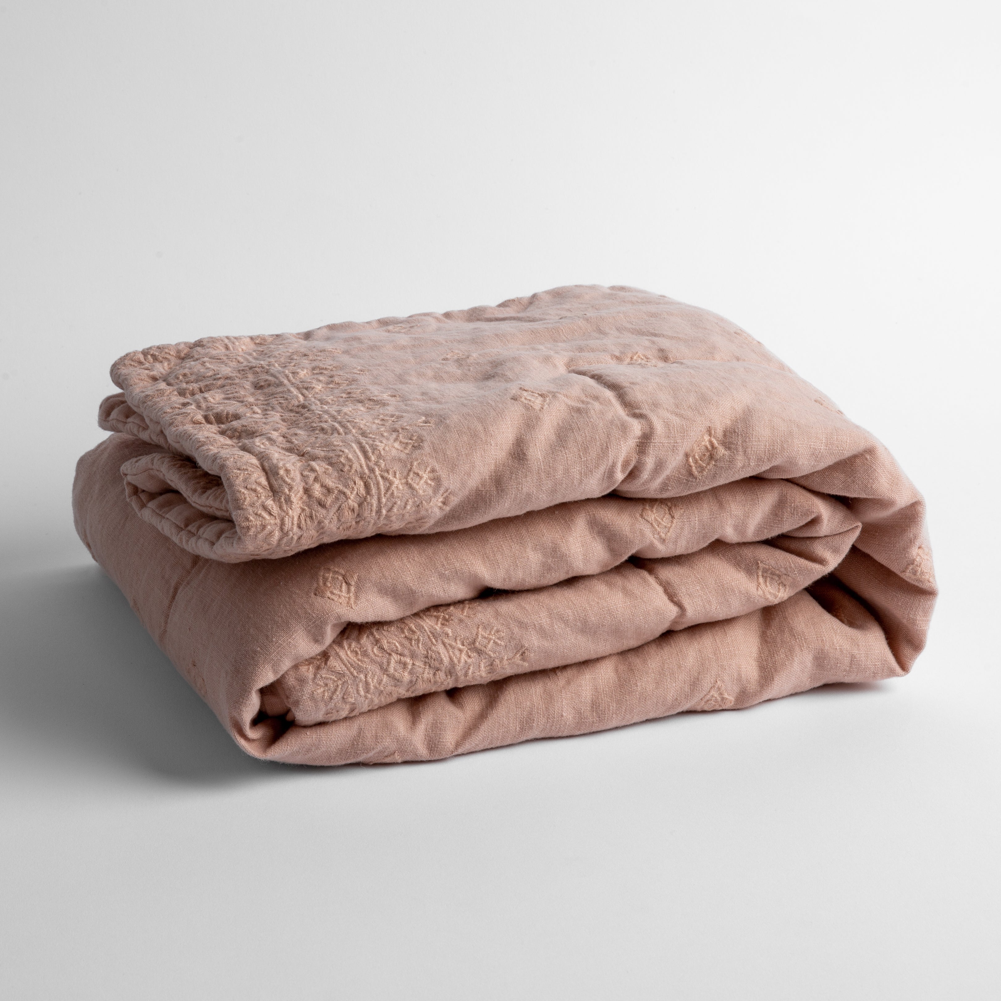 Rouge: embroidered linen baby blanket folded and shown  overhead from a slight angle against a white background. 