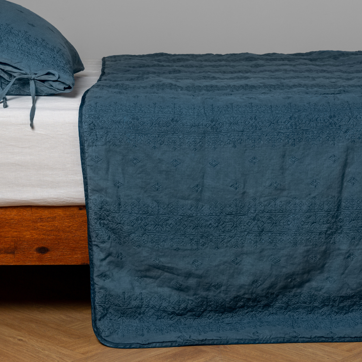Cenote: embroidered midweight linen bedspread with matching sham on a bed with a white fitted sheet. Shot from the side view, the bedframe is slightly visible  against a white background and medium wood floor. 