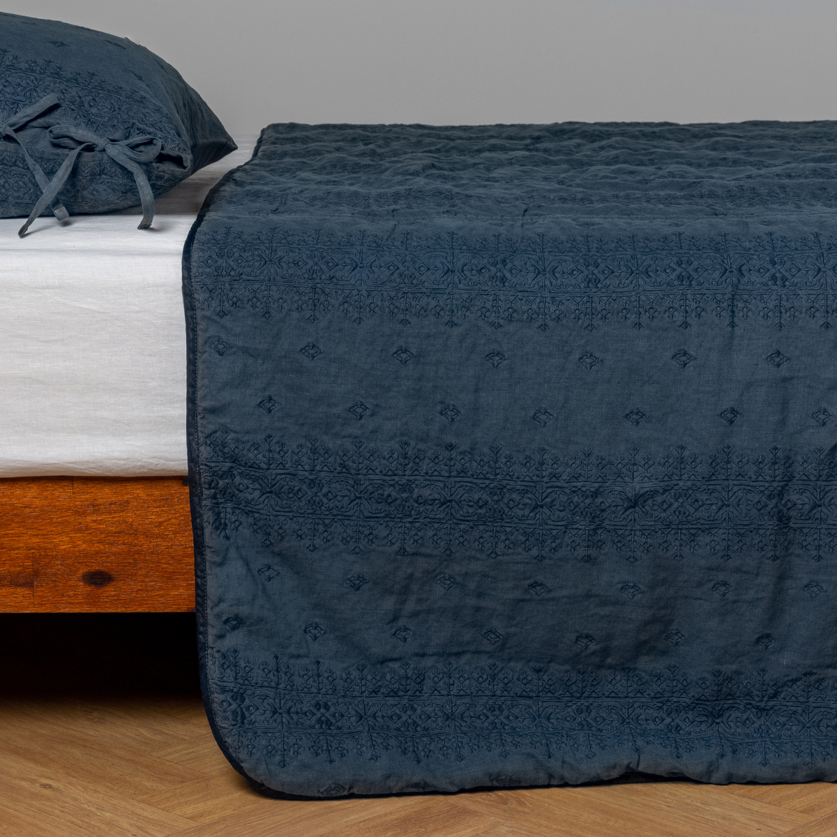Midnight:  embroidered midweight linen bedspread with matching sham on a bed with a white fitted sheet. Shot from the side view, the bedframe is slightly visible  against a white background and medium wood floor. 