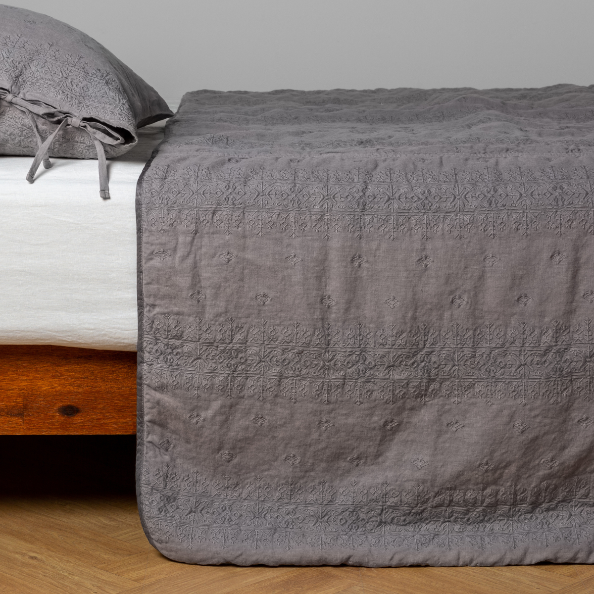 Moonlight:  embroidered midweight linen bedspread with matching sham on a bed with a white fitted sheet. Shot from the side view, the bedframe is slightly visible  against a white background and medium wood floor. 