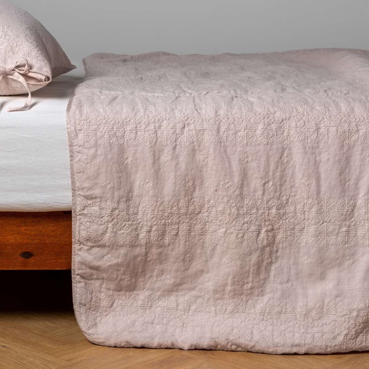 Pearl:  embroidered midweight linen bedspread with matching sham on a bed with a white fitted sheet. Shot from the side view, the bedframe is slightly visible  against a white background and medium wood floor. 