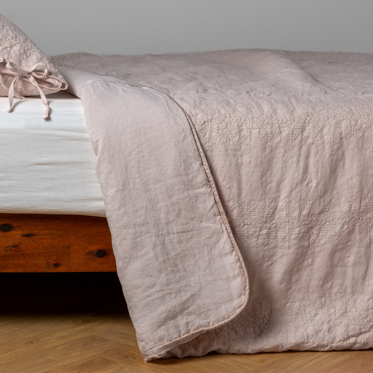 Pearl: White: embroidered bedspread with corner pulled back  showing the plain linen back. Shown with a white fitted sheet and matching sham, the bedframe is slightly visible  and the bed is against a white wall and on a medium wood floor. 
