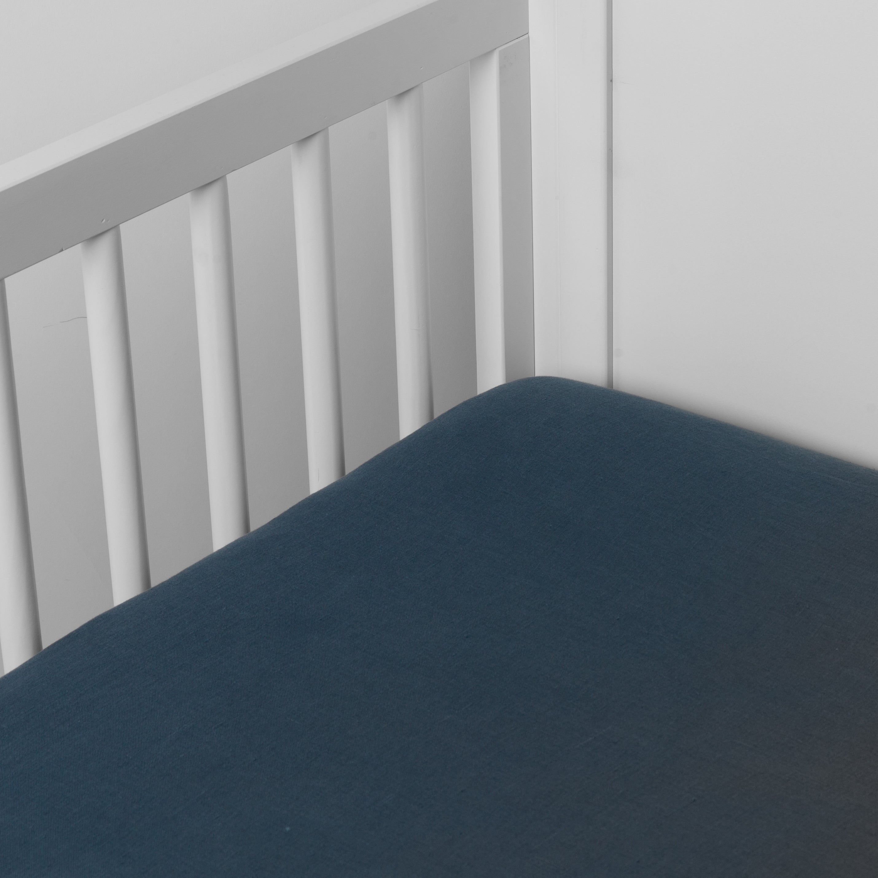 Midnight: linen crib sheet on the mattress shot slightly overhead into the corner of a white crib. against a white background. 