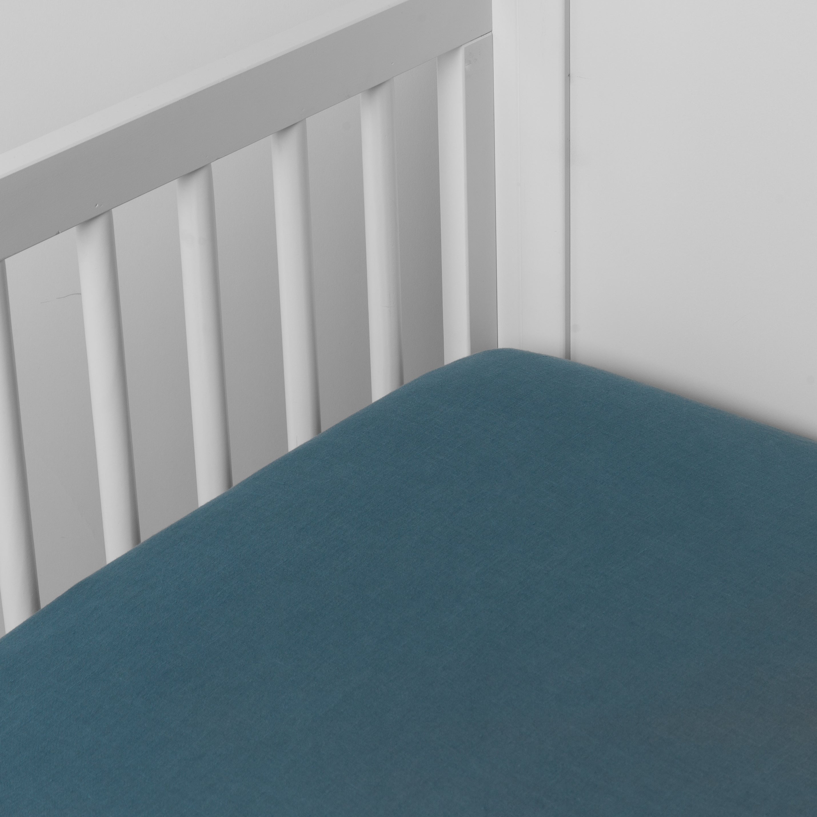 Cenote: linen crib sheet on the mattress shot slightly overhead into the corner of a white crib. against a white background. 