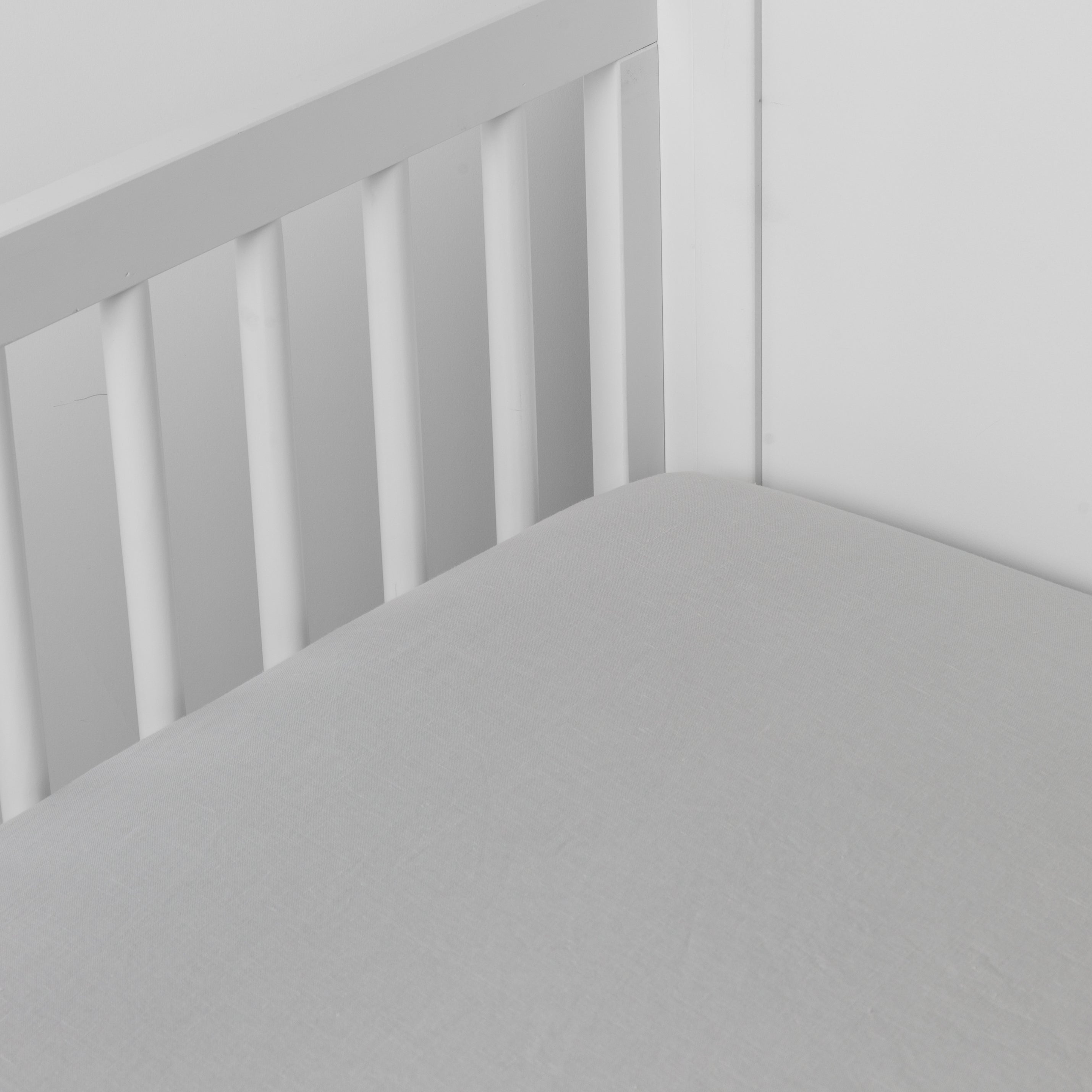 Cloud:  linen crib sheet on the mattress shot slightly overhead into the corner of a white crib. against a white background. 