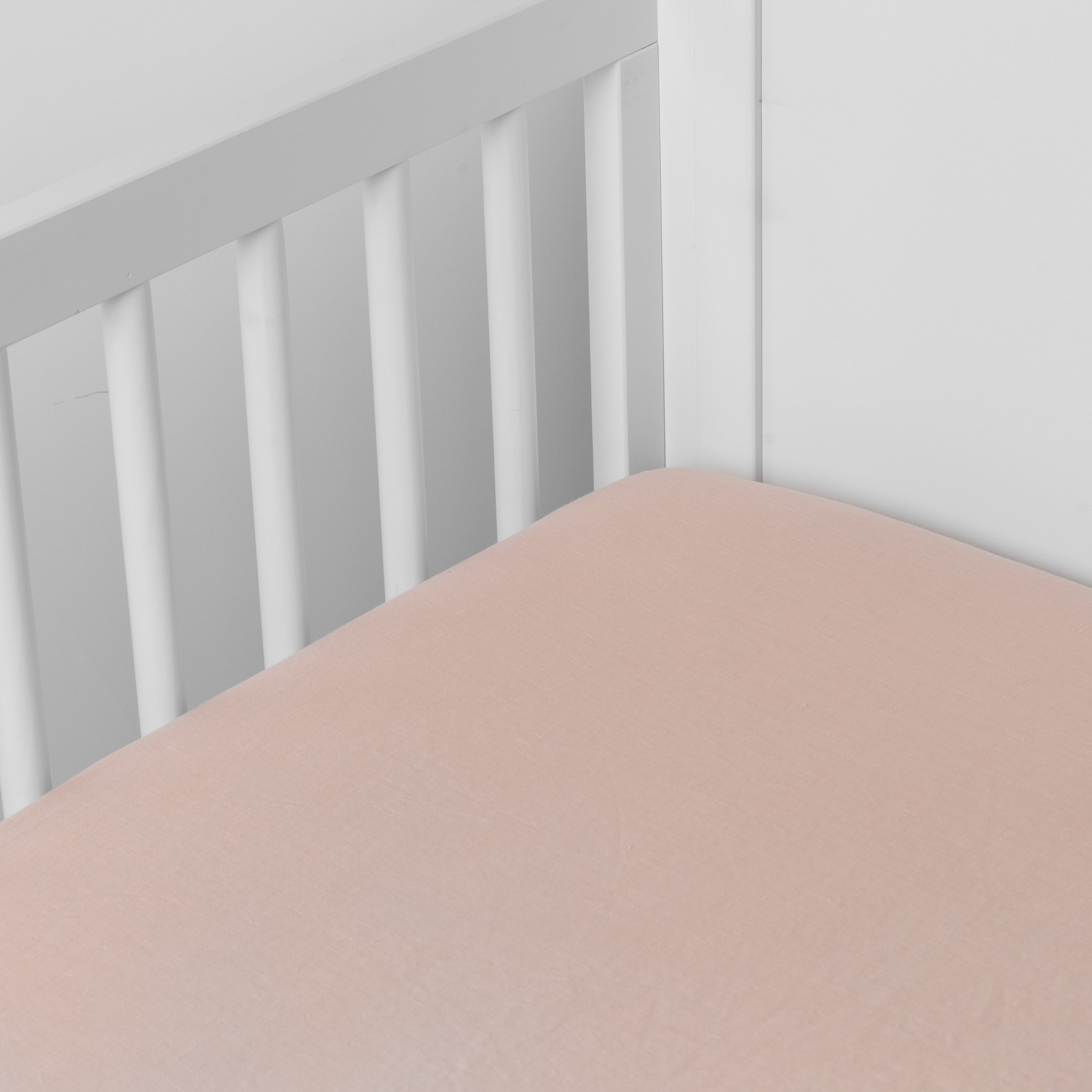 Pearl:  linen crib sheet on the mattress shot slightly overhead into the corner of a white crib. against a white background. 