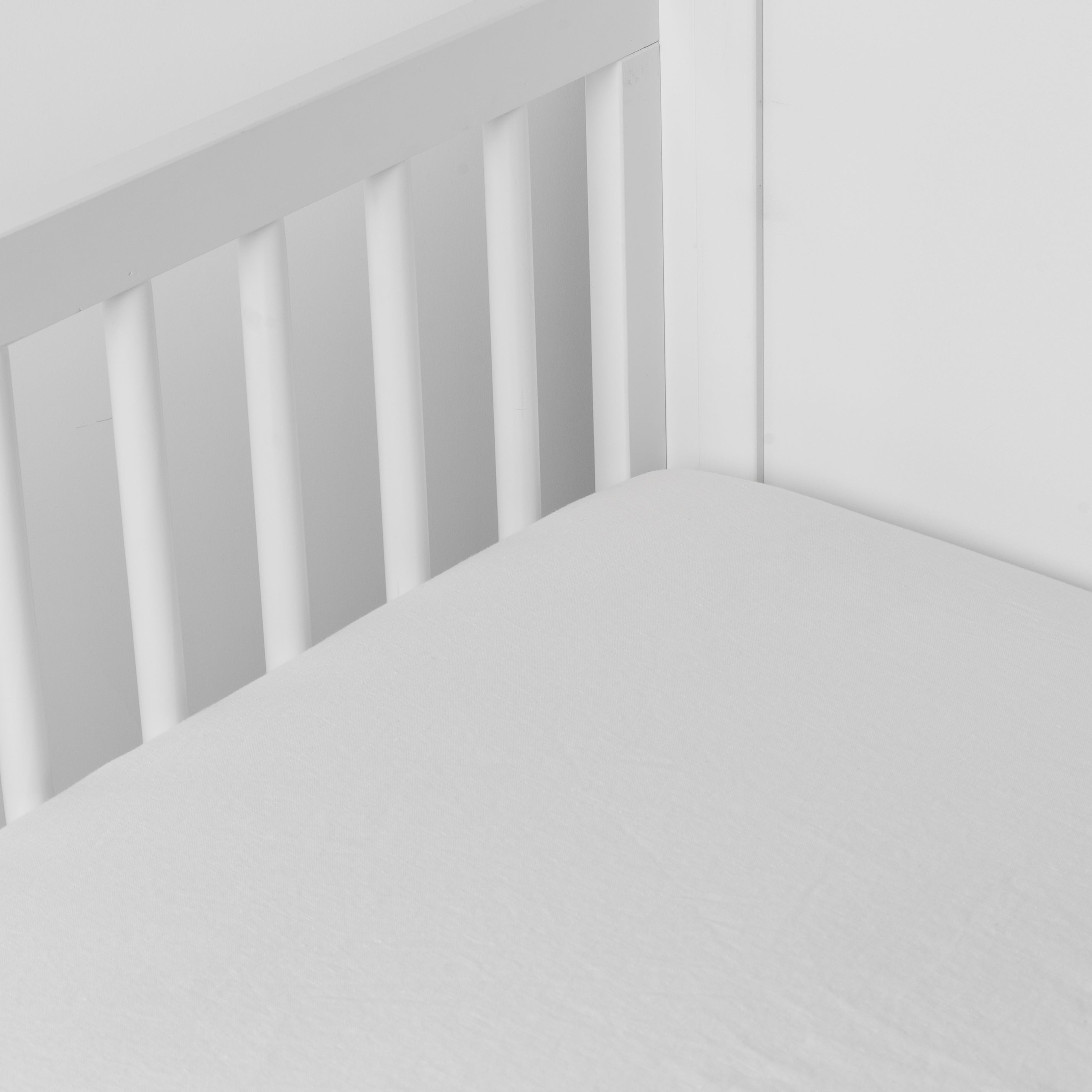 Winter White:  linen crib sheet on the mattress shot slightly overhead into the corner of a white crib. against a white background. 