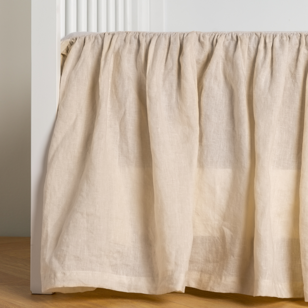 Parchment:  crib skirt shown on a white crib with no mattress against a white wall and medium wood flooring. 