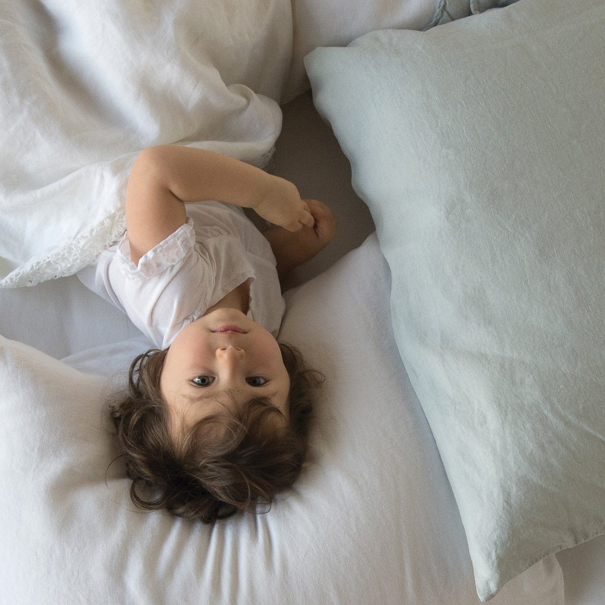 : A young toddler laying on a linen pillowcase and looking at the camera - overhead view.