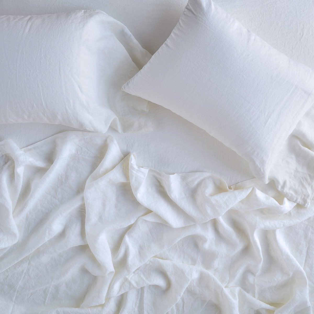 White: sleeping pillows laid flat on rumpled matching sheeting - overhead view.