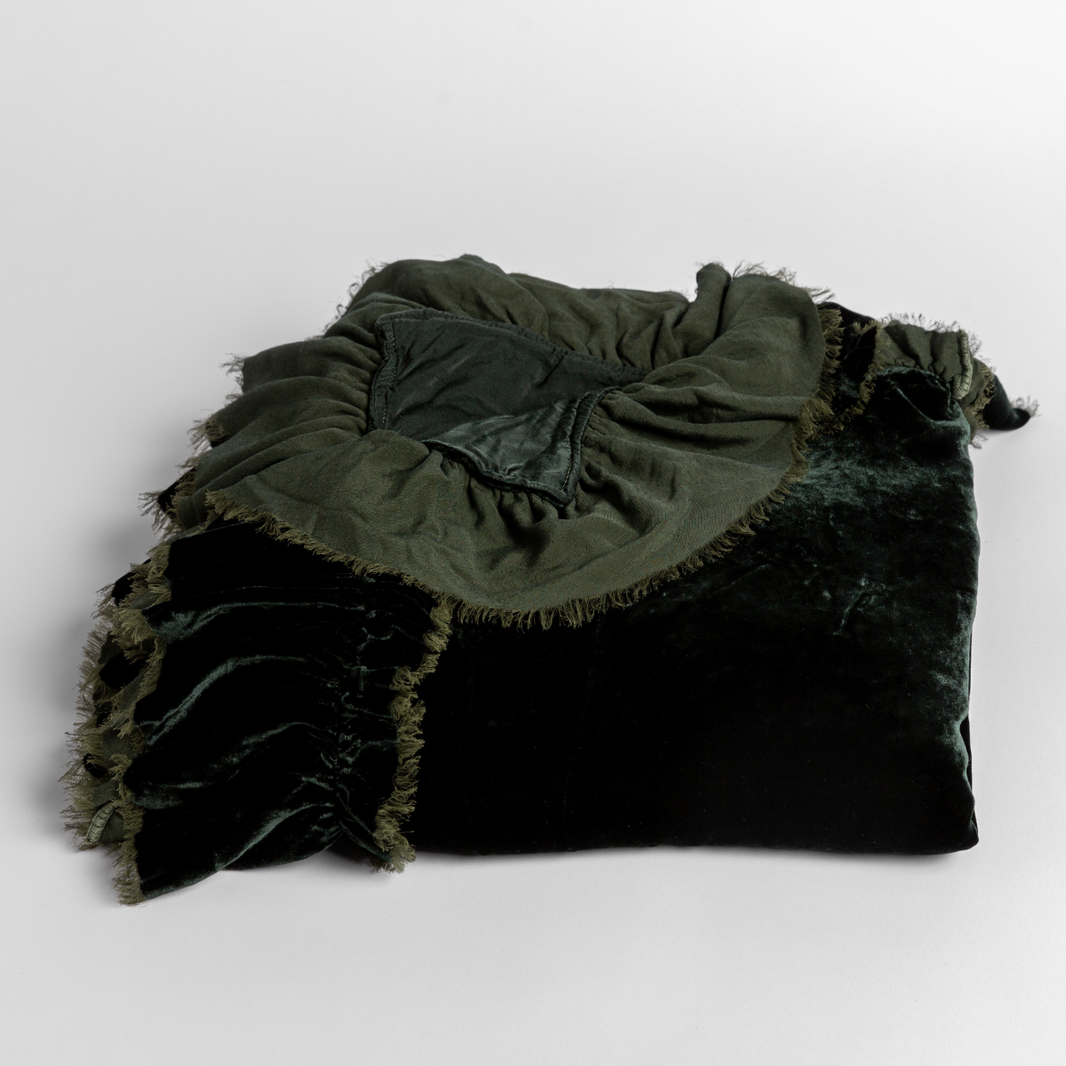 Juniper: silk velvet baby blanket with raw-edge ruffle folded with a corner pulled back, shown slightly overhead and against a white background. 