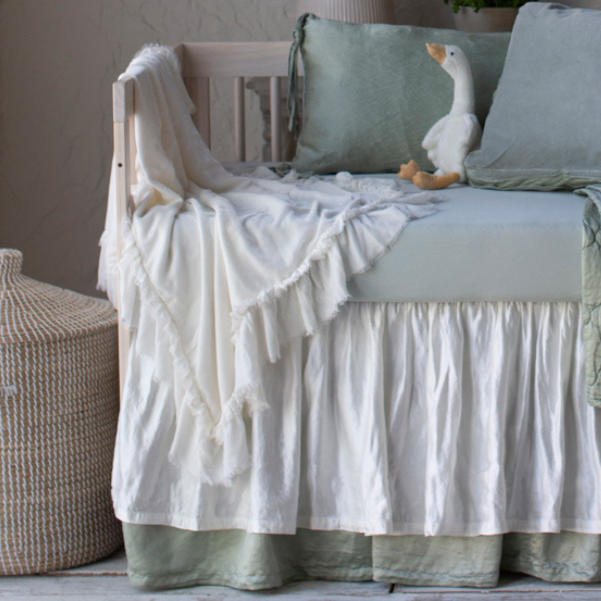 [allvariants]: Silk velvet blanket in winter white, draped over the front and side of a crib with soft green and white bedding.