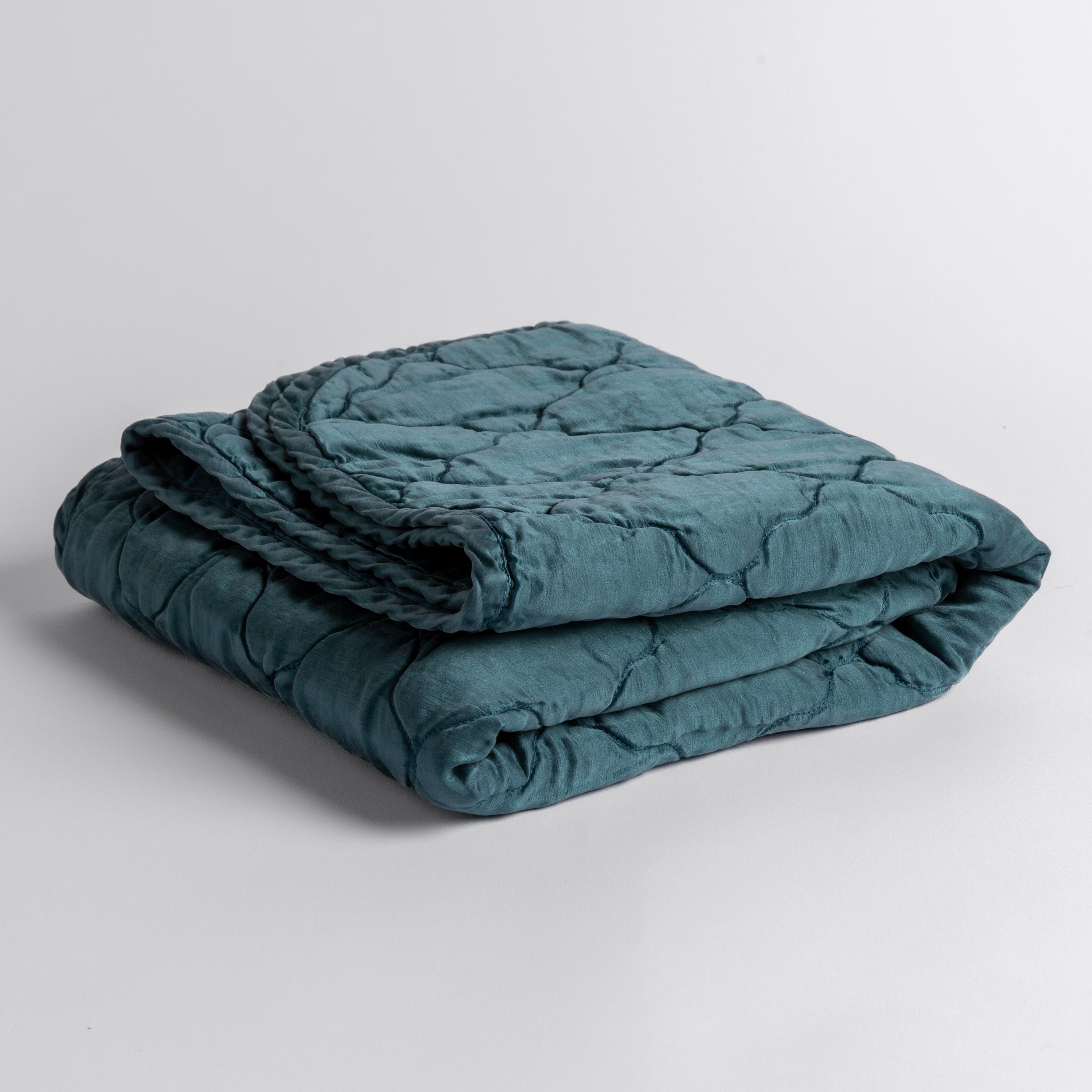 Cenote:  quilted charmeuse blanket folded and shown against a white background from a slight overhead angle. 