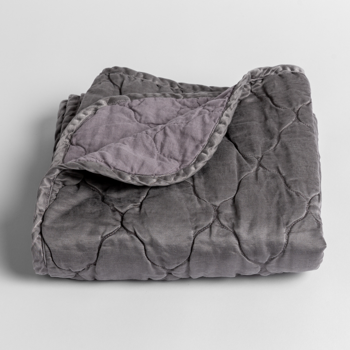 French Lavender: quilted charmeuse blanket folded with a corner folded back to show the contrast of the linen back - shown slightly overhead against a white background. 