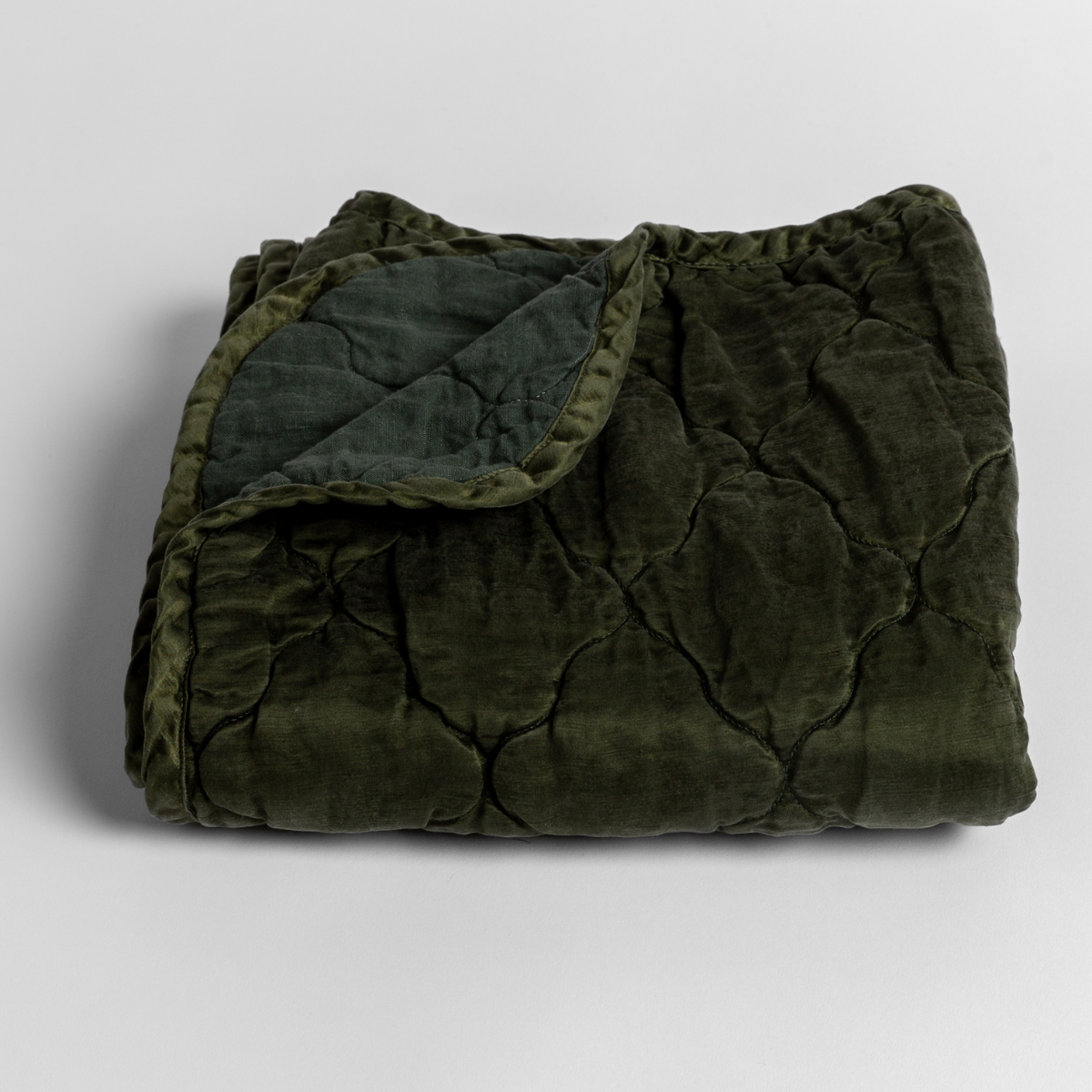 Juniper: quilted charmeuse blanket folded with a corner pulled back to show the linen back - slightly overhead against a white background. 