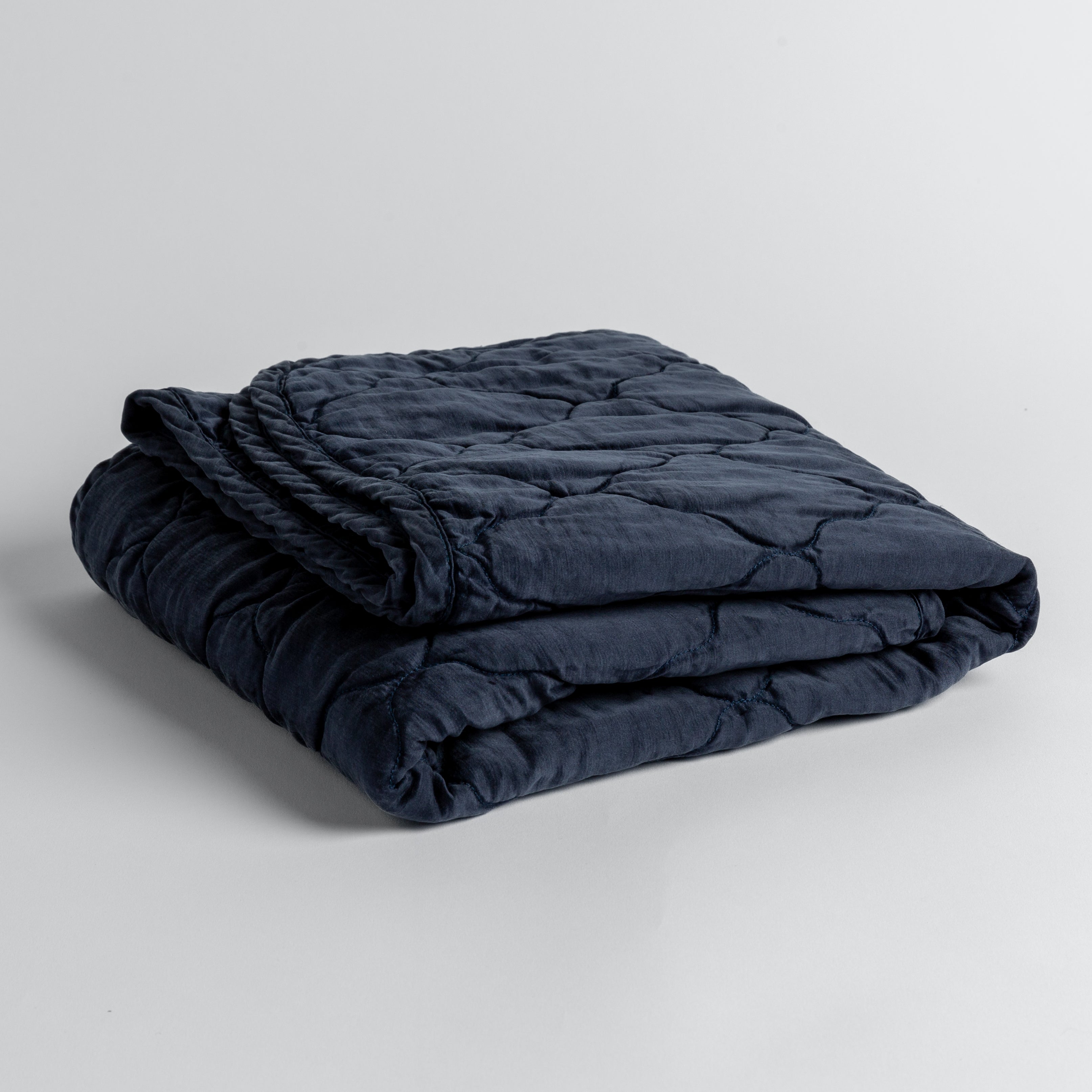 Midnight:  quilted charmeuse blanket folded and shown against a white background from a slight overhead angle. 