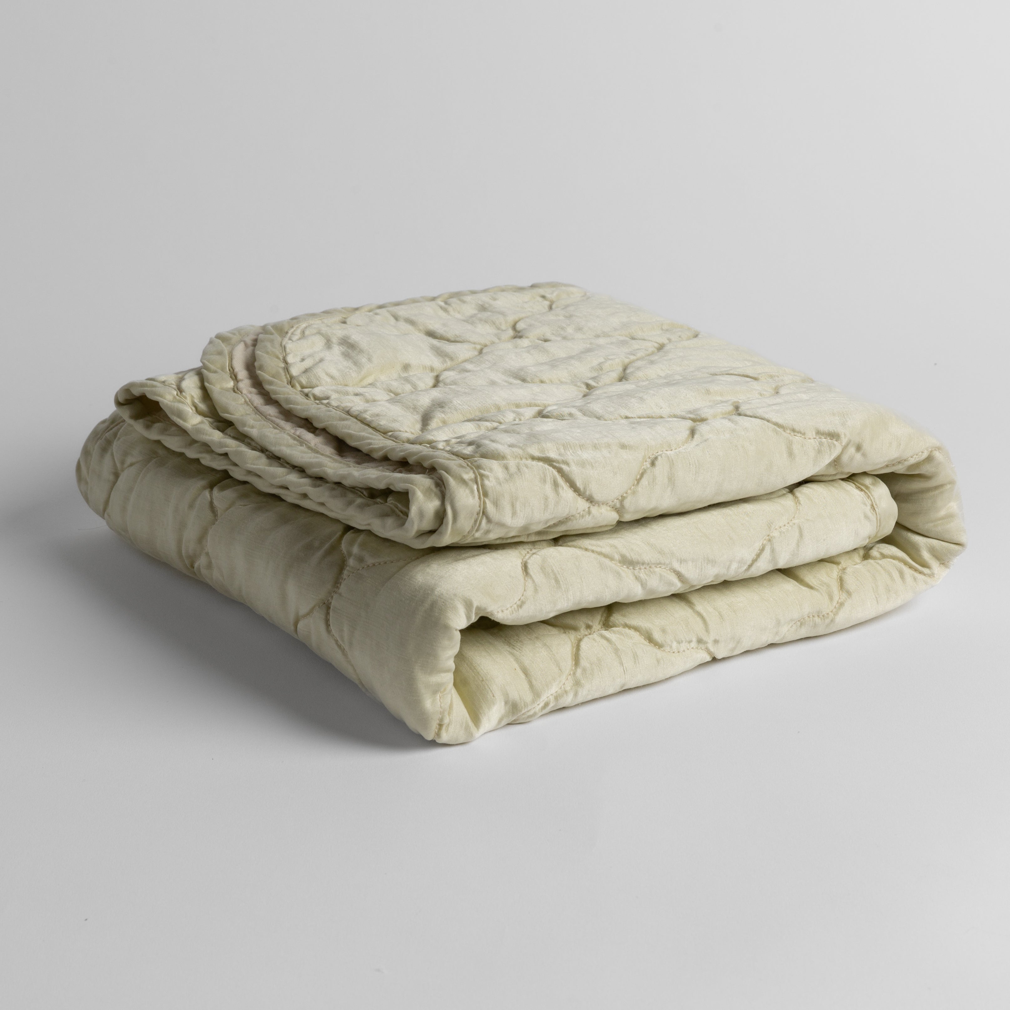 Parchment:  quilted charmeuse blanket folded and shown against a white background from a slight overhead angle. 