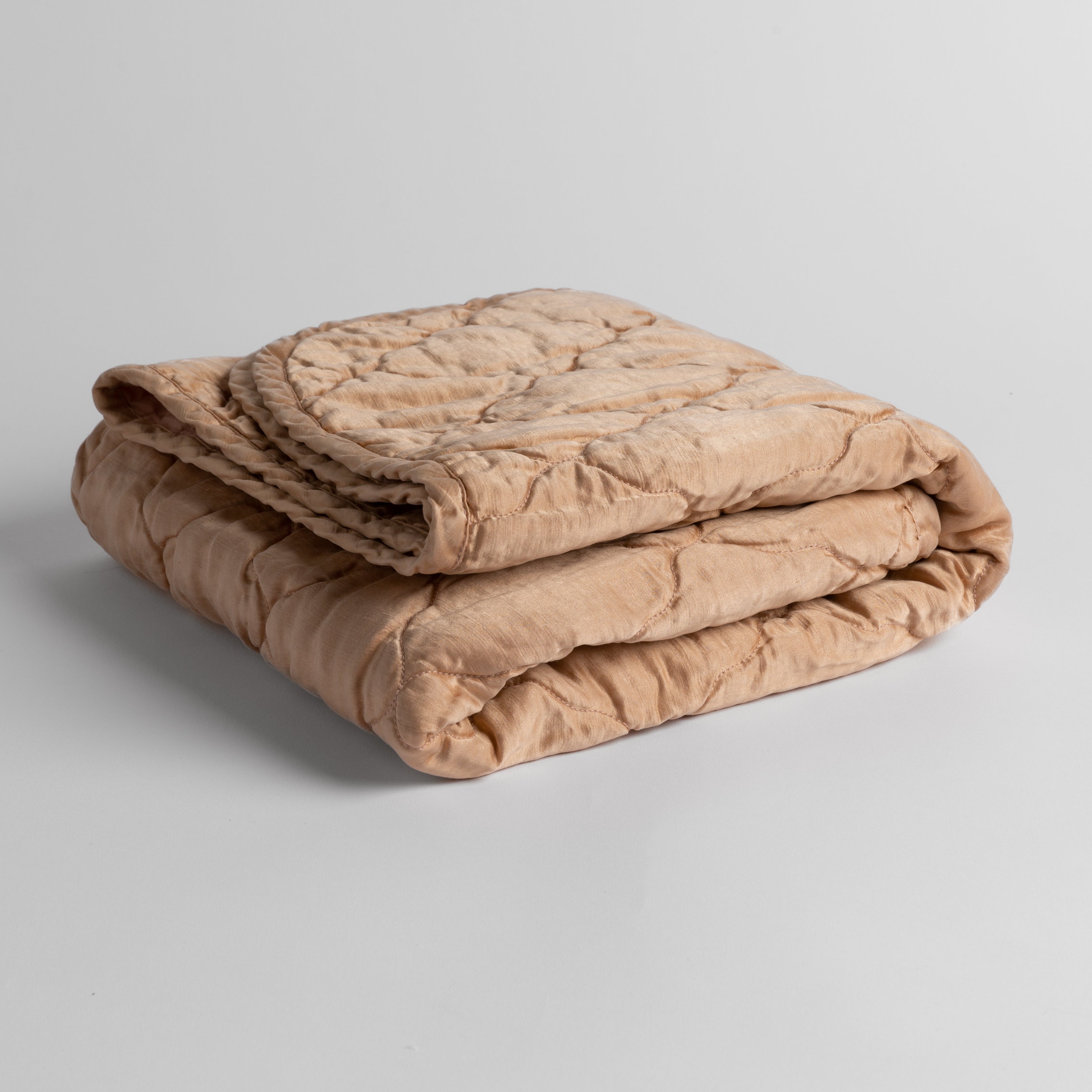 Rouge: quilted charmeuse blanket folded and shown against a white background from a slight overhead angle. 