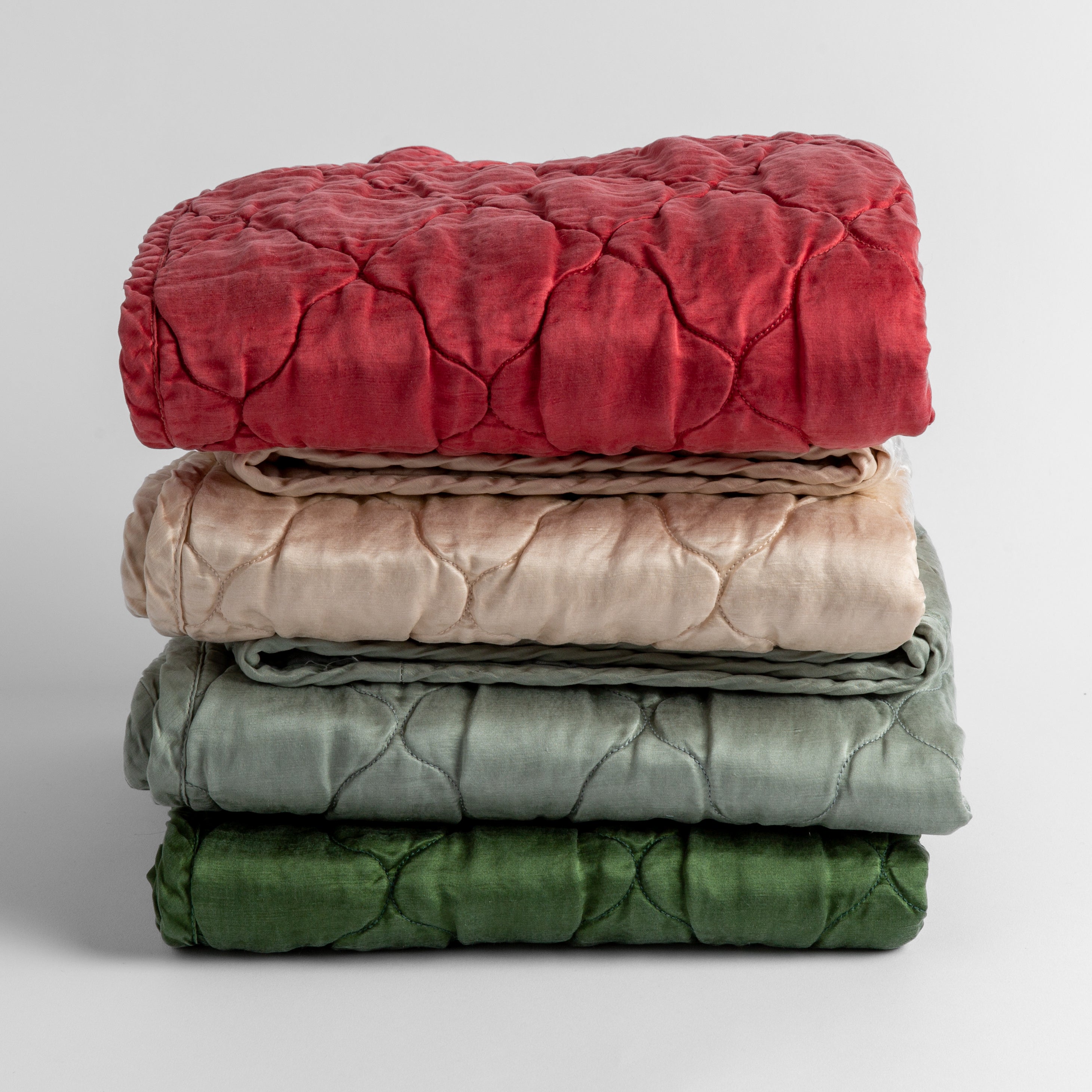 A stack of four quilted silk charmeuse baby blankets shown straight on against a white background. Blankets shown in Poppy, Pearl, Mineral and Jade.
