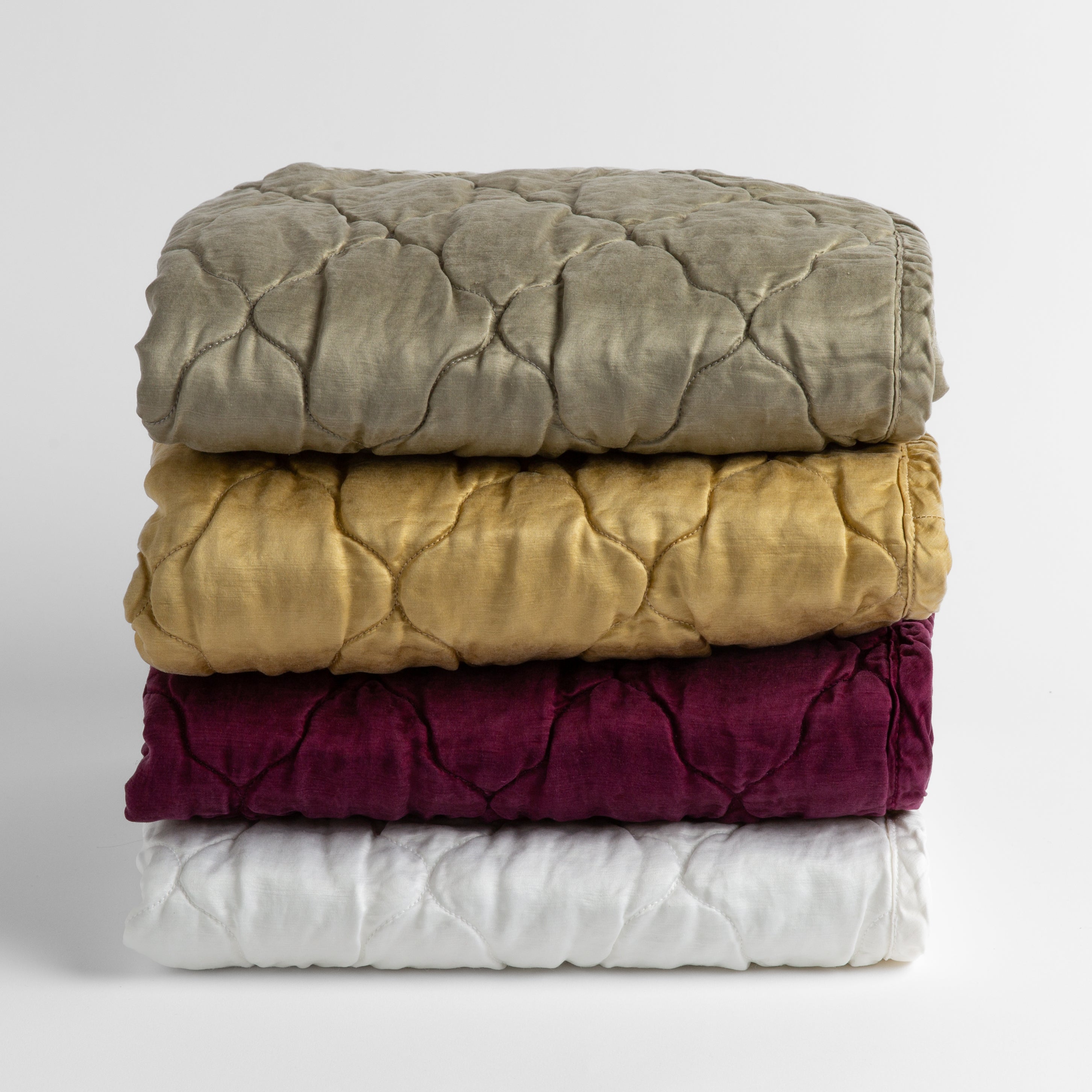 A stack of four quilted silk charmeuse baby blankets shown straight on against a white background. Blankets shown in Moonlight, Honeycomb, Fig and White.