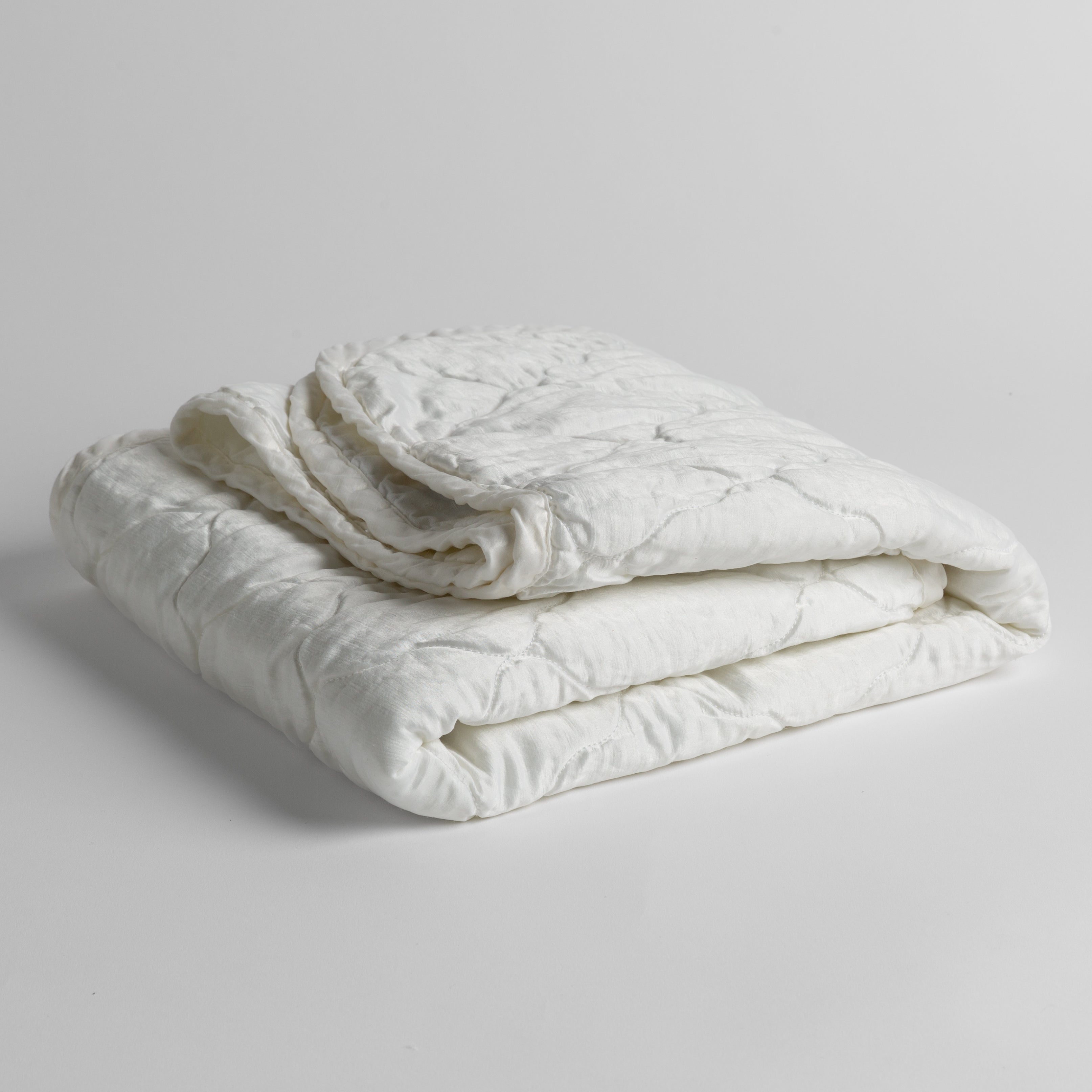 White: quilted charmeuse blanket folded and shown against a white background from a slight overhead angle. 