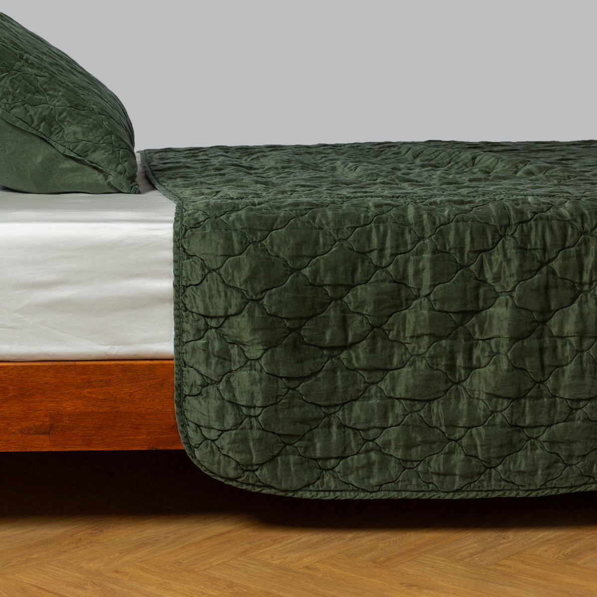 quilted charmeuse coverlet shown with a matching sham from the luna collection shown on a bed with a winter white fitted sheet - side view. 