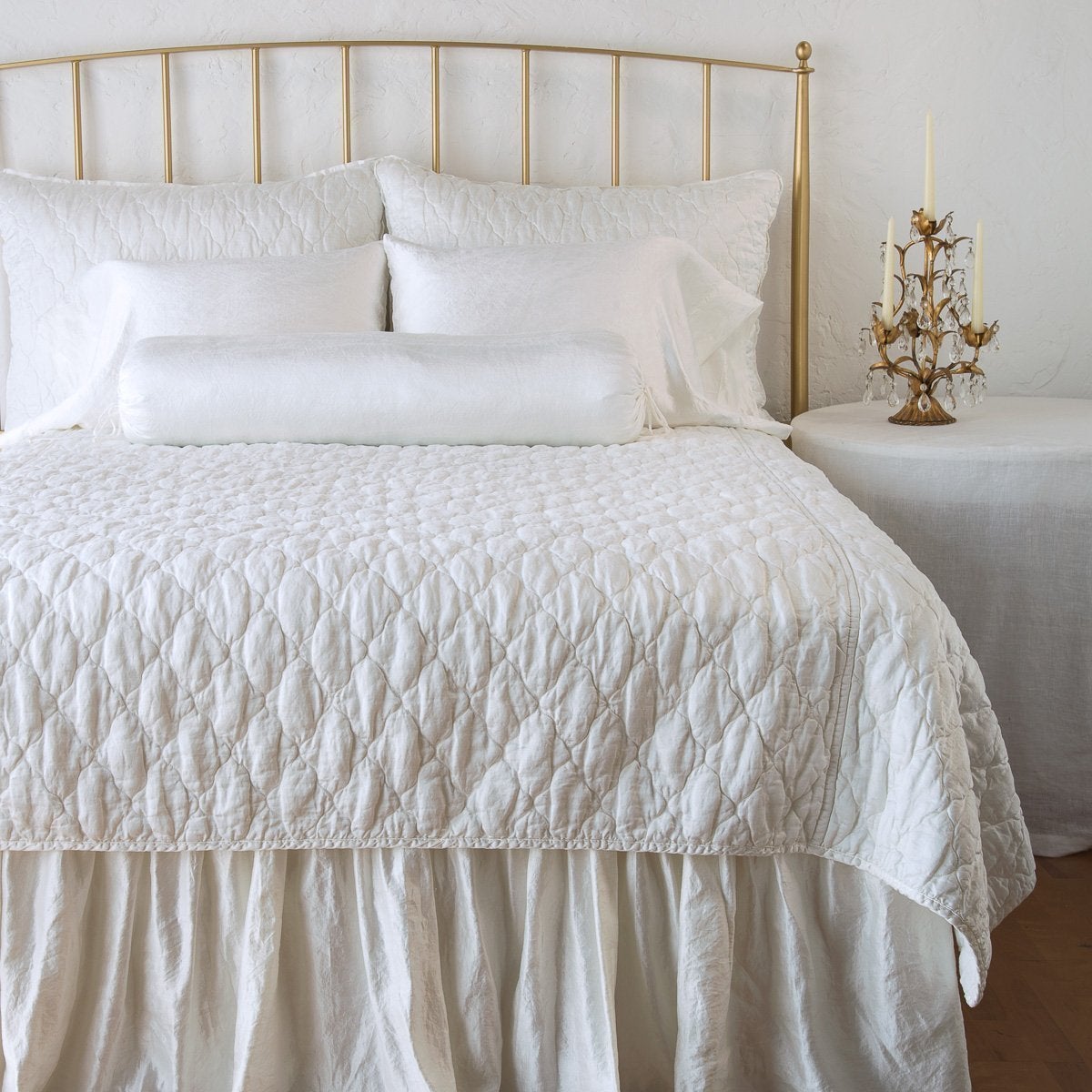 [allvariants]: Luna coverlet on a shining, monochromatic bed with matching shams and charmeuse pillows and bed skirt - winter white, end of bed view.
