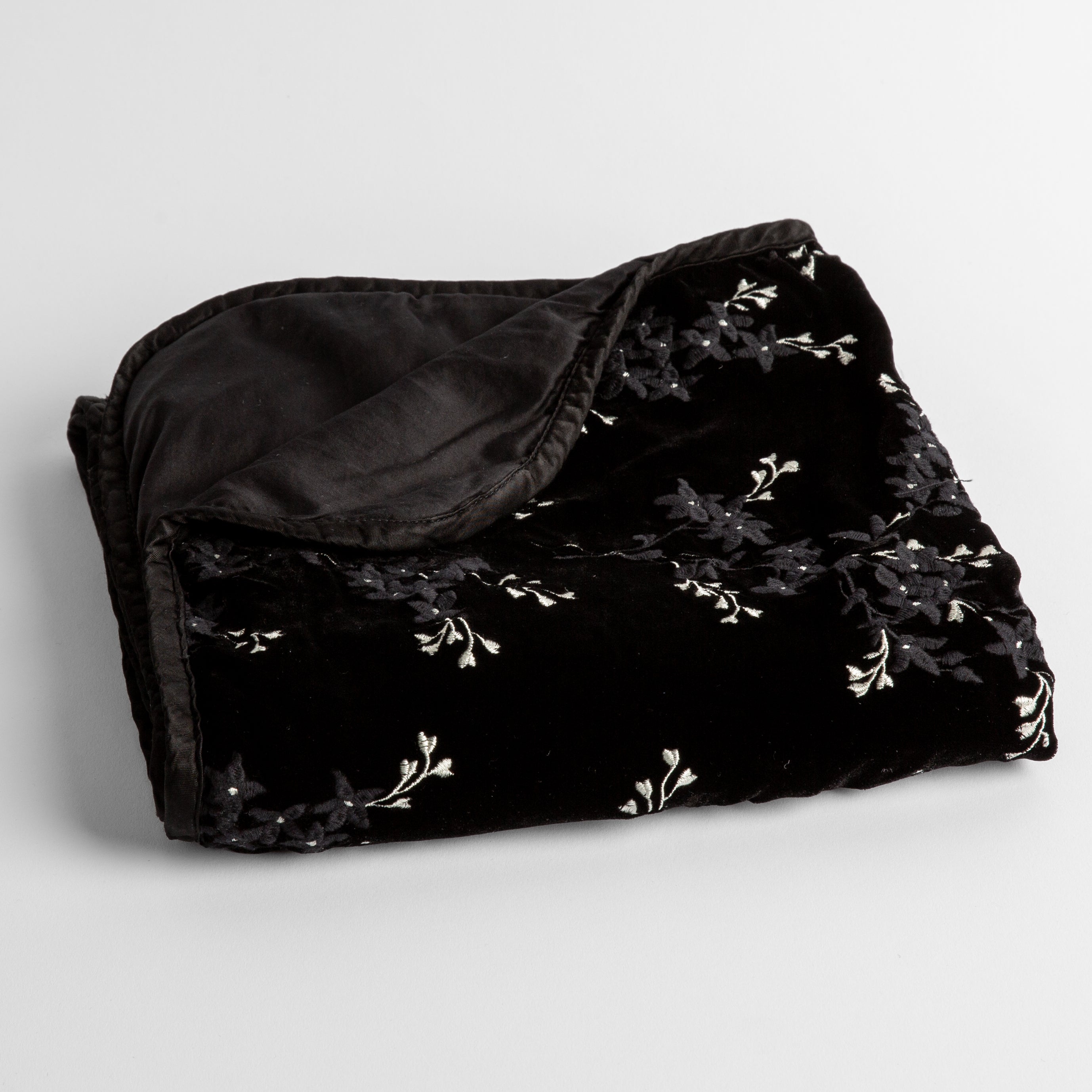 Corvino: embroidered silk velvet baby blanket folded with a corner folded back to show the trim and back of the blanket - shot overhead at a slight angle against a white background. 