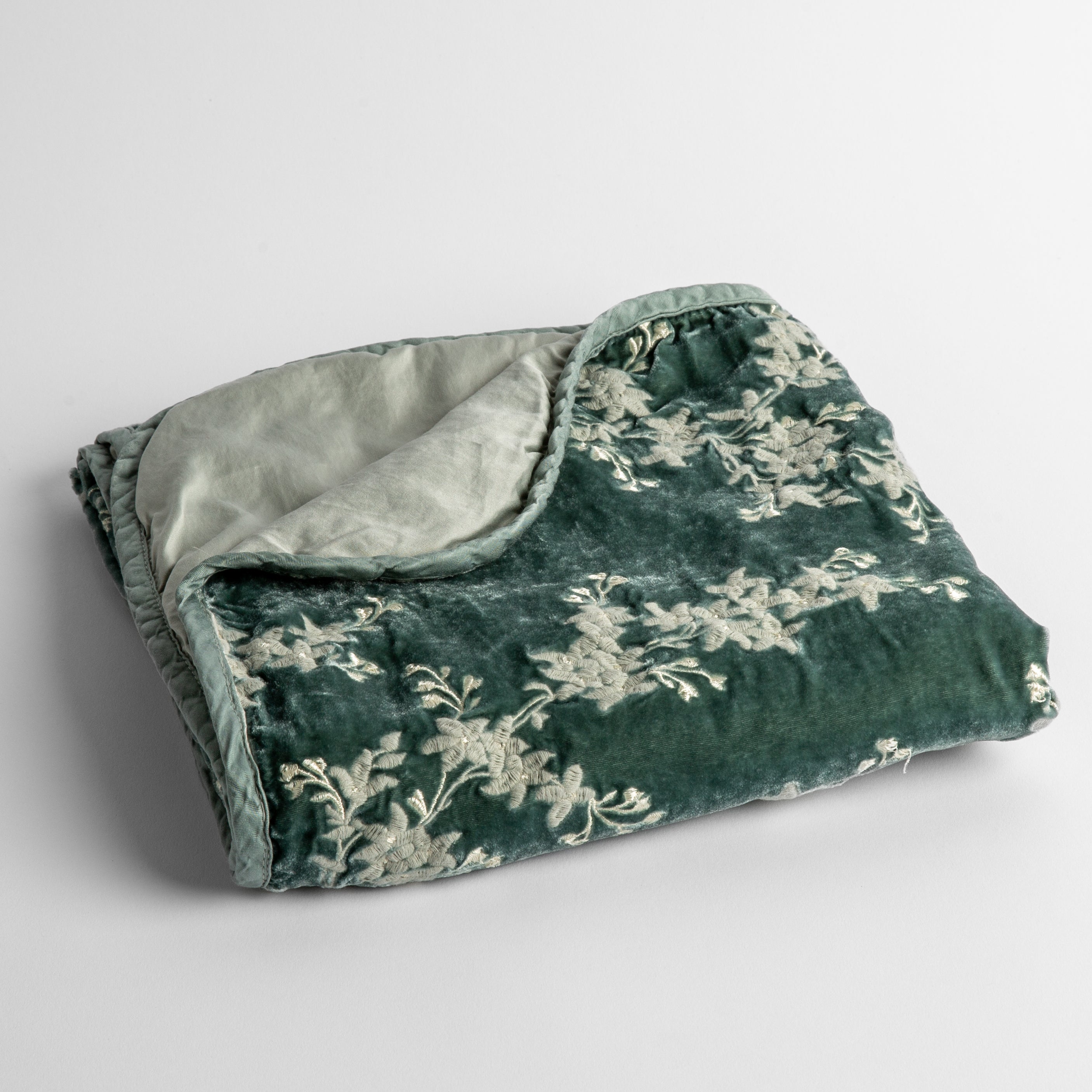 Eucalyptus: embroidered silk velvet baby blanket folded with a corner folded back to show the trim and back of the blanket - shot overhead at a slight angle against a white background. 