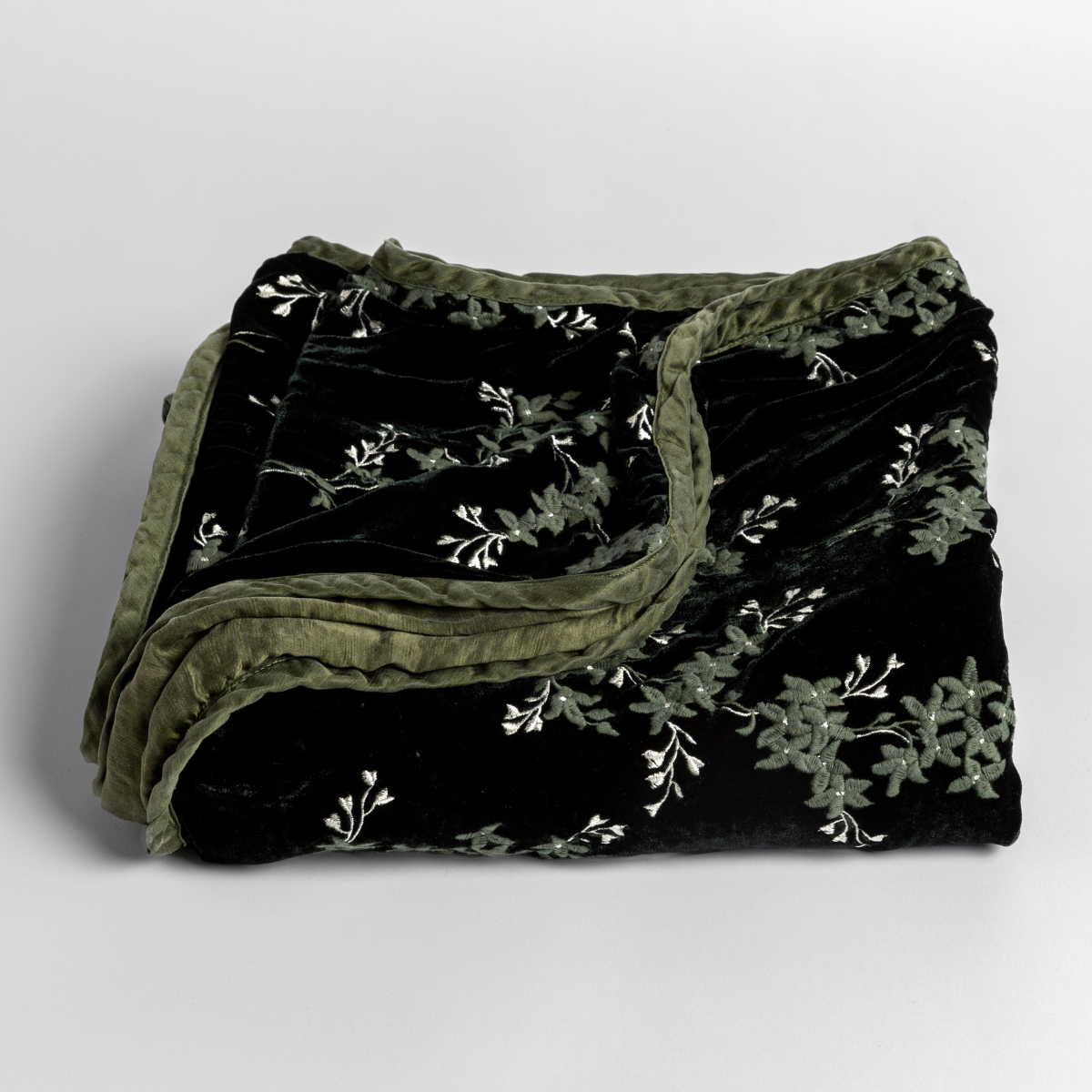 Juniper: embroidered silk velvet blanket folded with its corners pulled down to show the trim detail - slightly overhead against a white background. 
