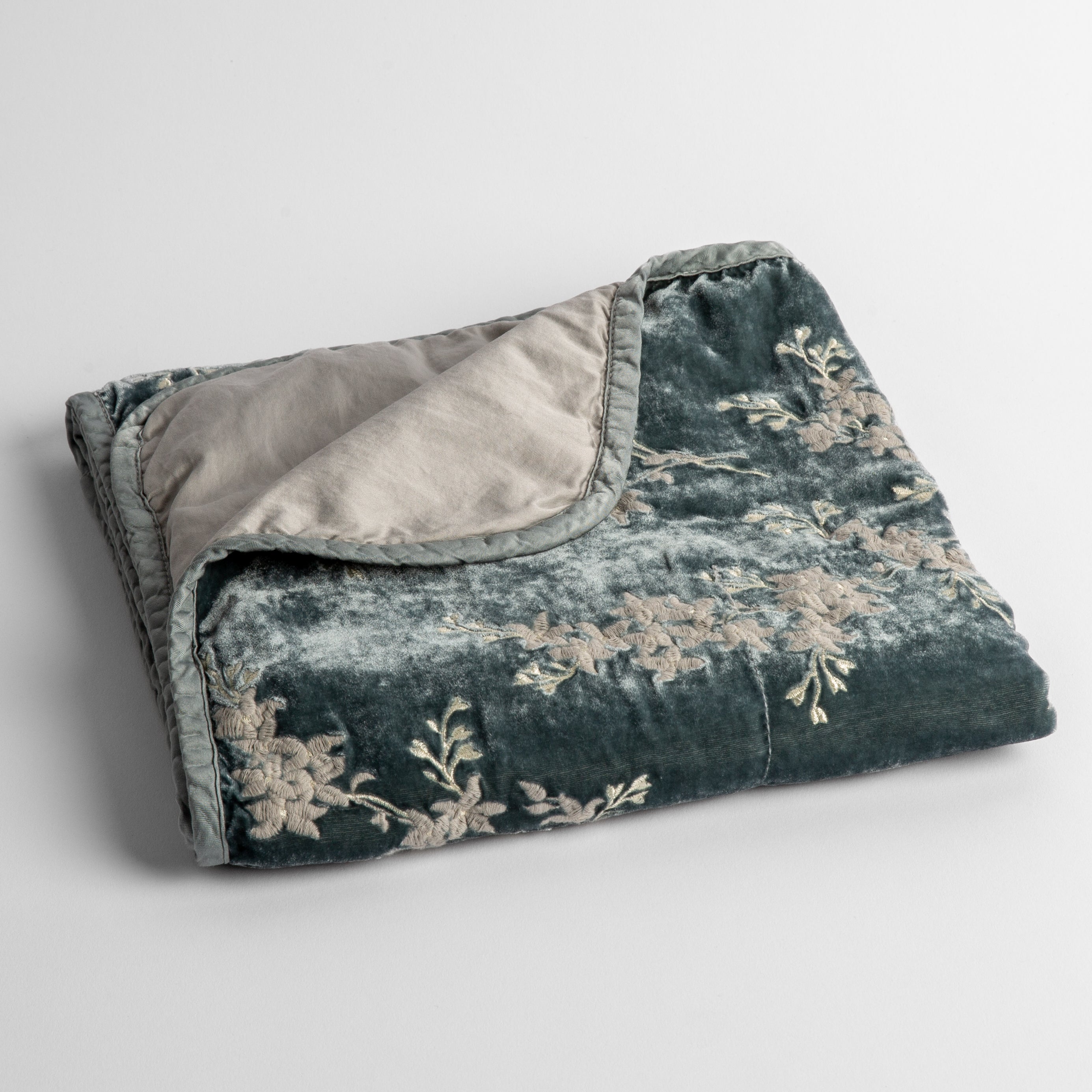 Mineral: embroidered silk velvet baby blanket folded with a corner folded back to show the trim and back of the blanket - shot overhead at a slight angle against a white background. 