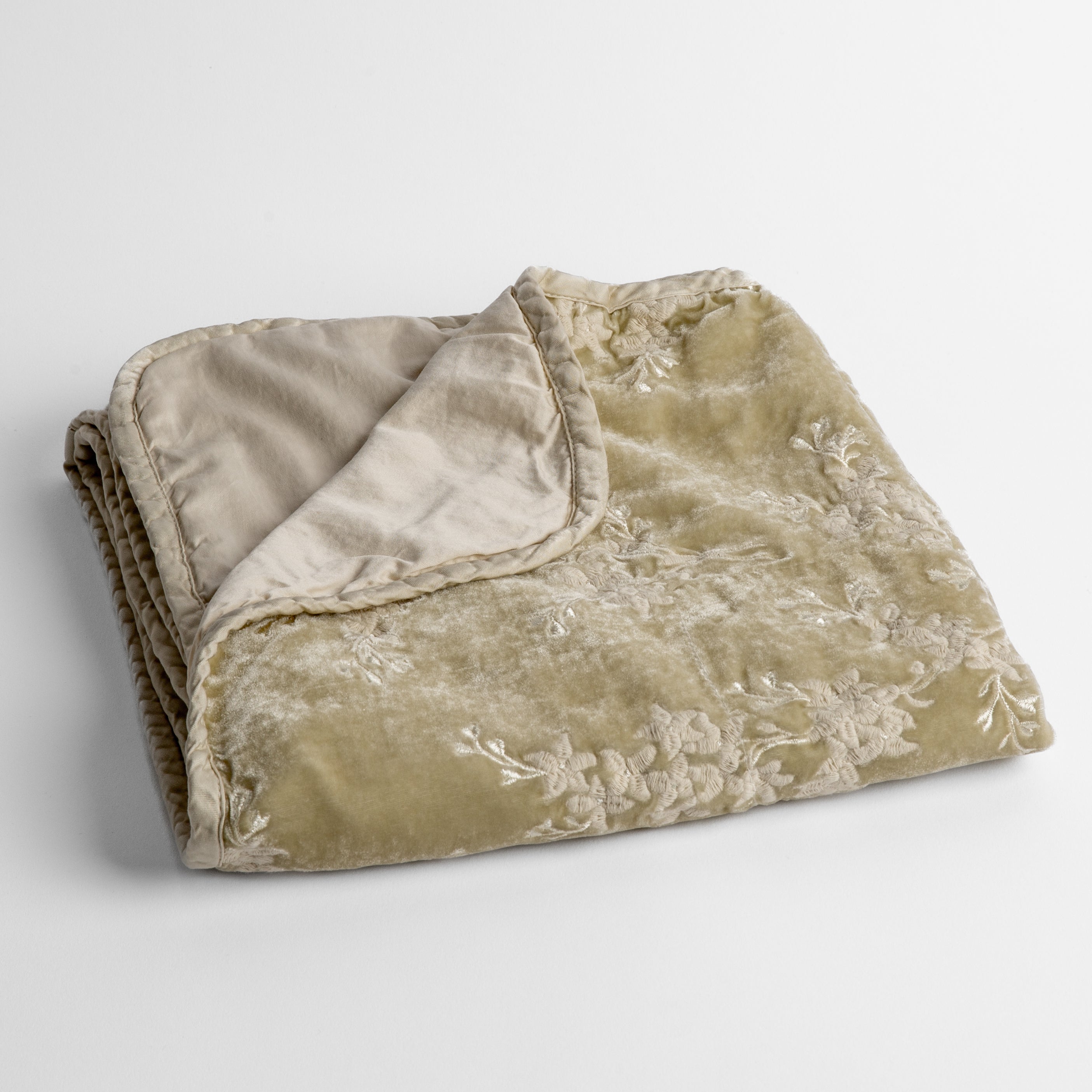 Parchment: embroidered silk velvet baby blanket folded with a corner folded back to show the trim and back of the blanket - shot overhead at a slight angle against a white background. 