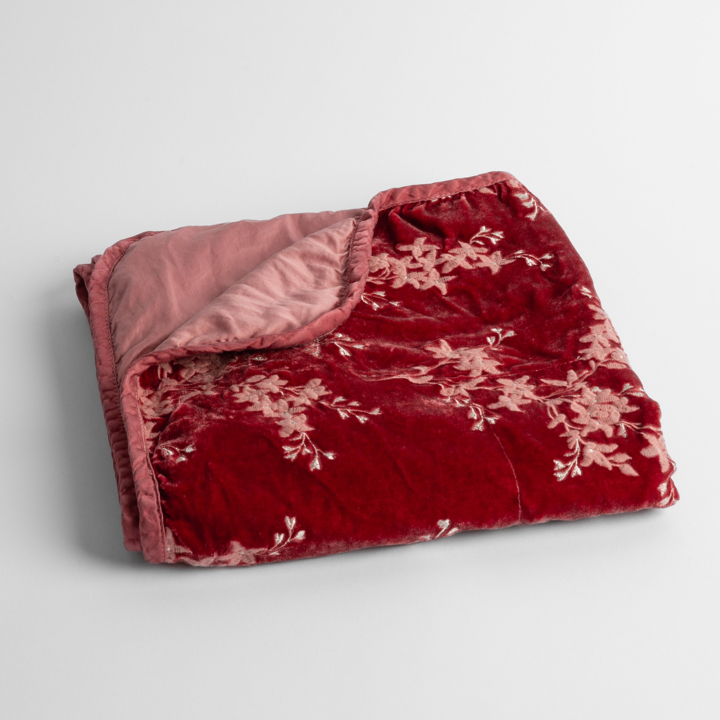 Poppy: embroidered silk velvet baby blanket folded with a corner folded back to show the trim and back of the blanket - shot overhead at a slight angle against a white background. 
