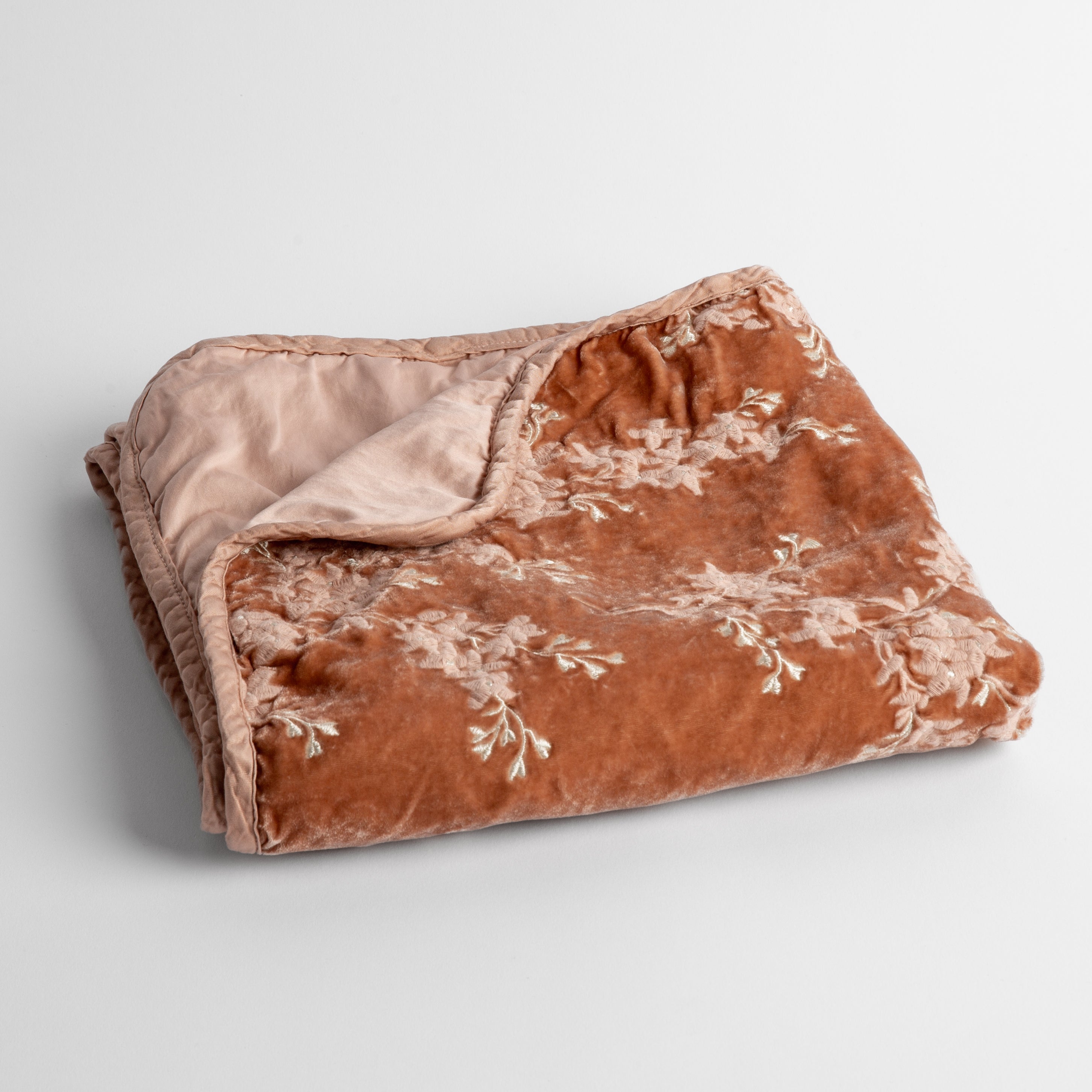 Rouge: embroidered silk velvet baby blanket folded with a corner folded back to show the trim and back of the blanket - shot overhead at a slight angle against a white background. 