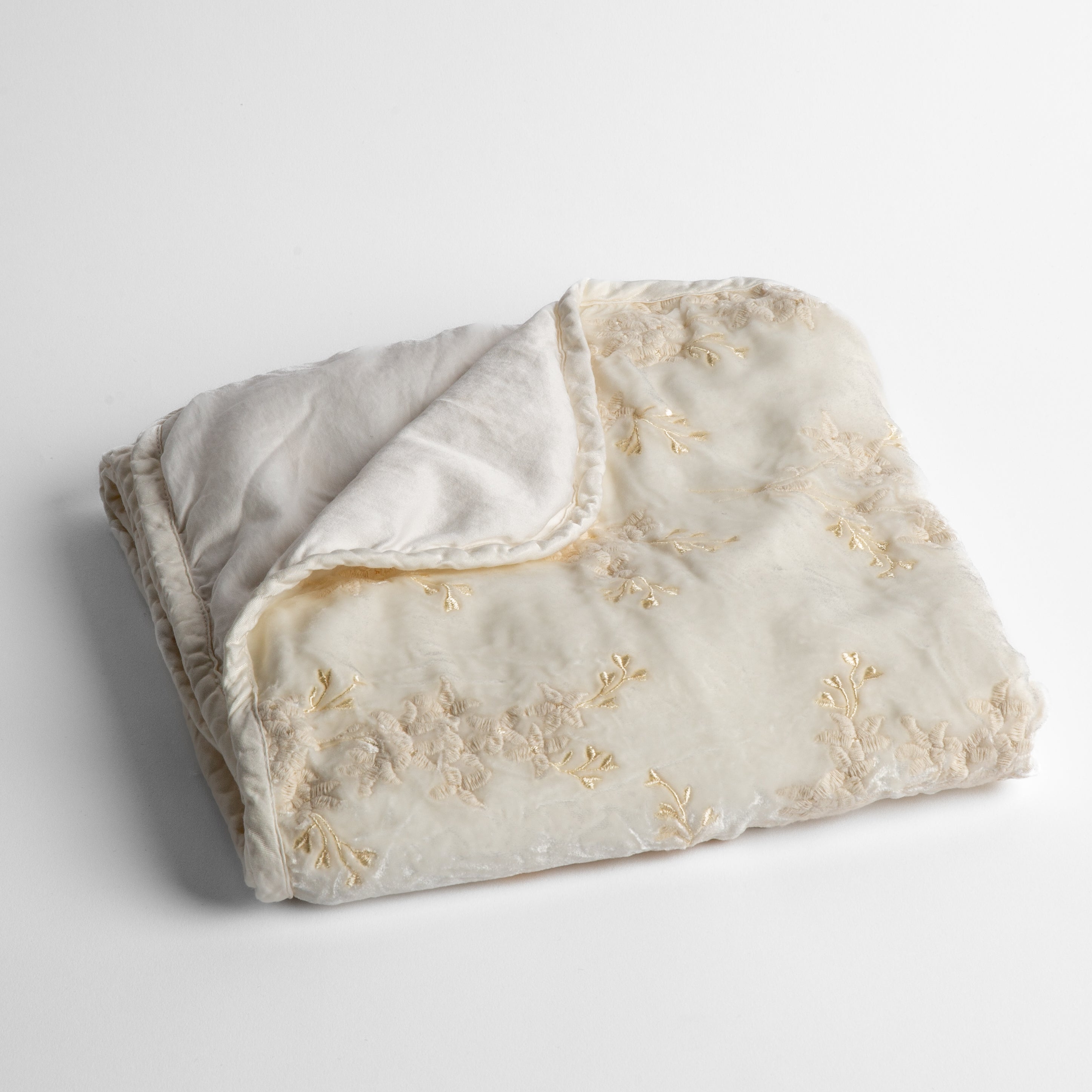 Winter White:  embroidered silk velvet baby blanket folded with a corner folded back to show the trim and back of the blanket - shot overhead at a slight angle against a white background. 
